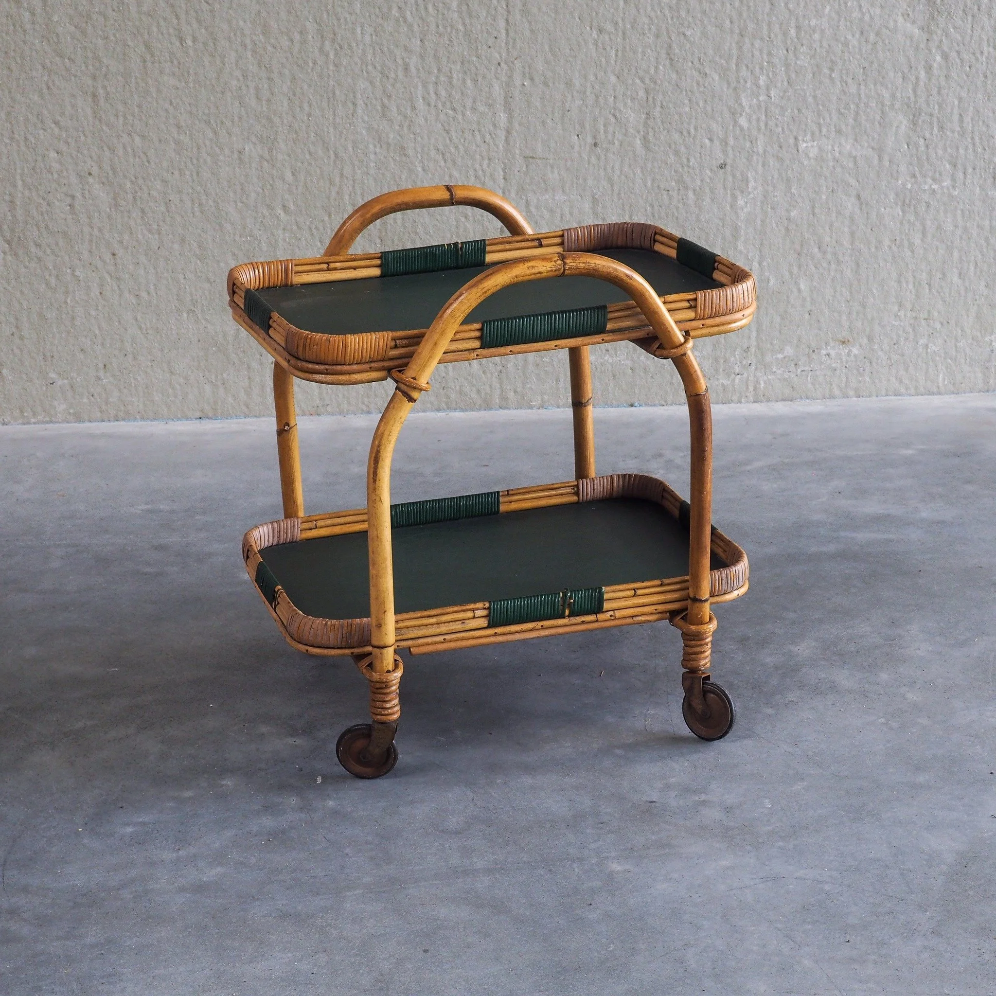 Vintage Bamboo Serving Trolley

Original 1950s bamboo serving trolley/ bar cart. Crafted with warm, bent bamboo framing and distinct deep green wrapping accents. It features two fully removable tier trays with dark surfaces, making serving drinks or 
