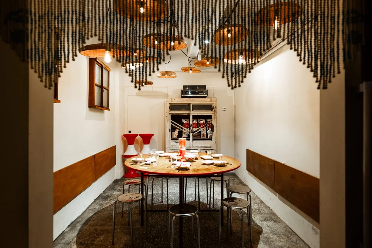 蒸籠化作吊燈，珠簾垂落如時間流動，為空間帶來獨特節奏。大圓桌承載著台灣辦桌文化的熱鬧與共享精神，搭配鐵椅、舊窗與老式碗櫥，喚起人們對街頭喜宴與社區記憶的共鳴。