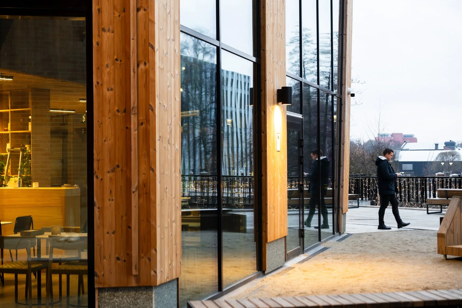 Facade Materiality and Public Space The exterior facade presents a warm, tactile expression through its cladding of heat-treated pine wood, contrasting with the stark lines of its neighbors. This design extends to the ground level, which was transfor