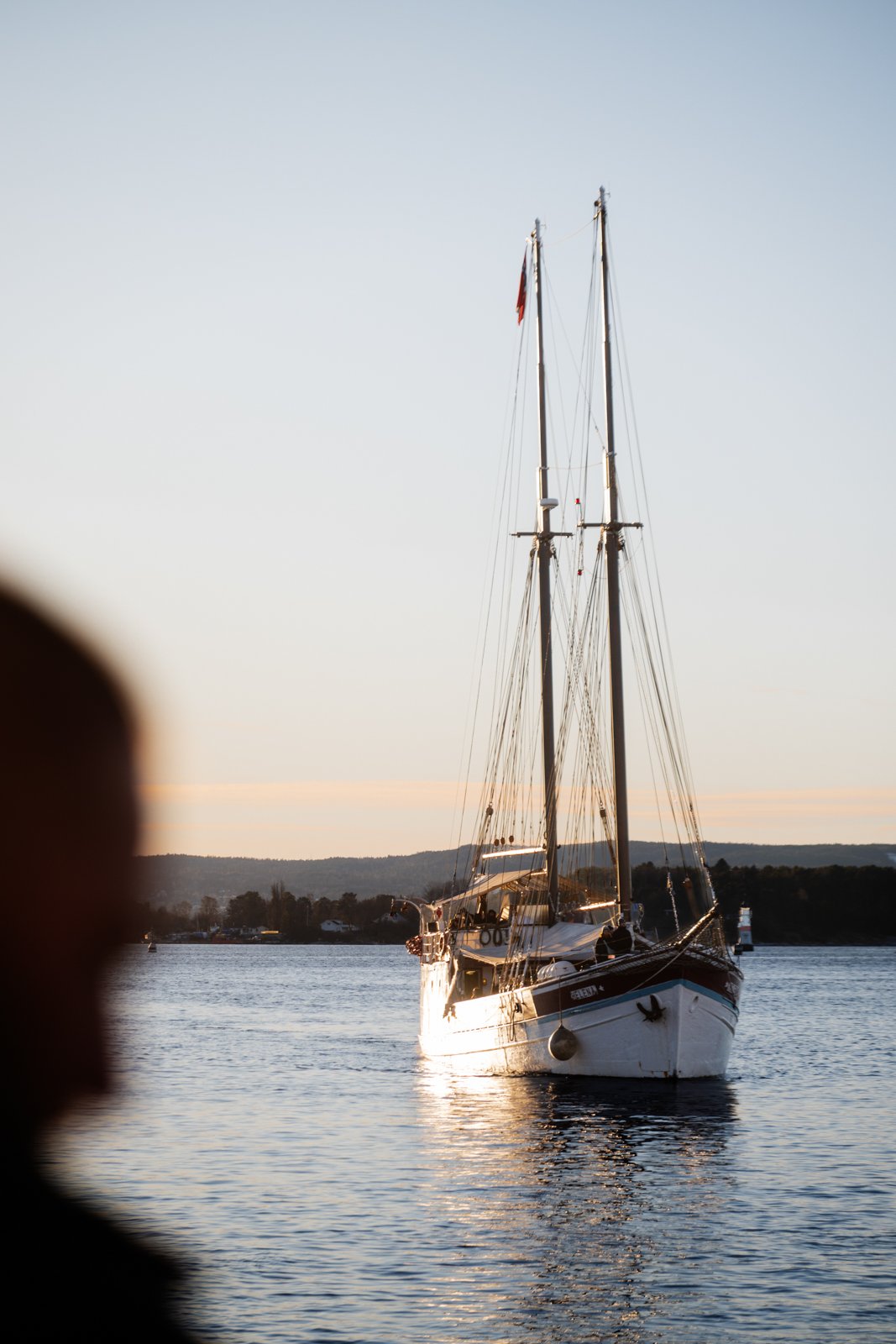 A sailboat on calm water during sunset with a silhouette of a person's face in the foreground.