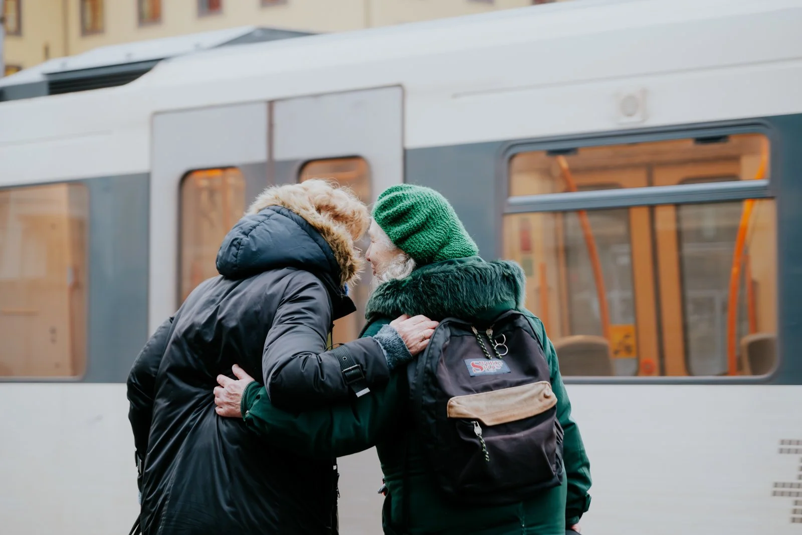 Two elderly people sharing a kiss or intimate moment on a city street, standing in front of a train.
