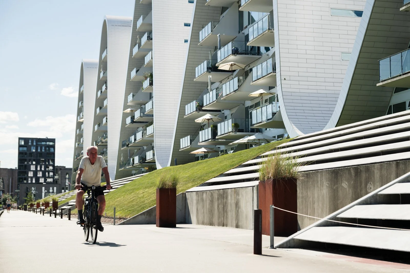The stepped public terrace leads up to the residential complex, showing the contrast between the linear steps and the organic wave form.