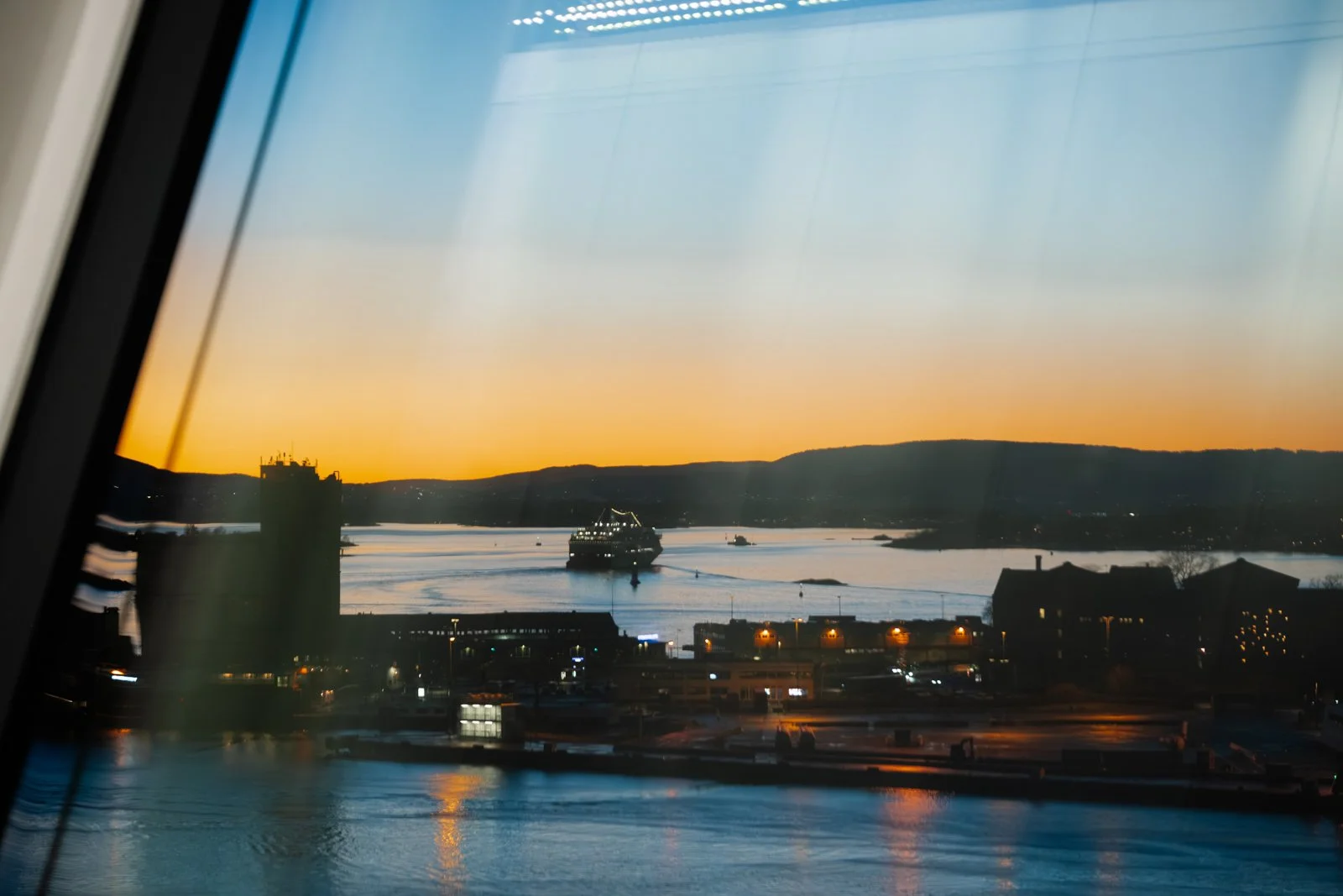 Photo of a sunset over a river with a boat in the water and buildings along the shore.
