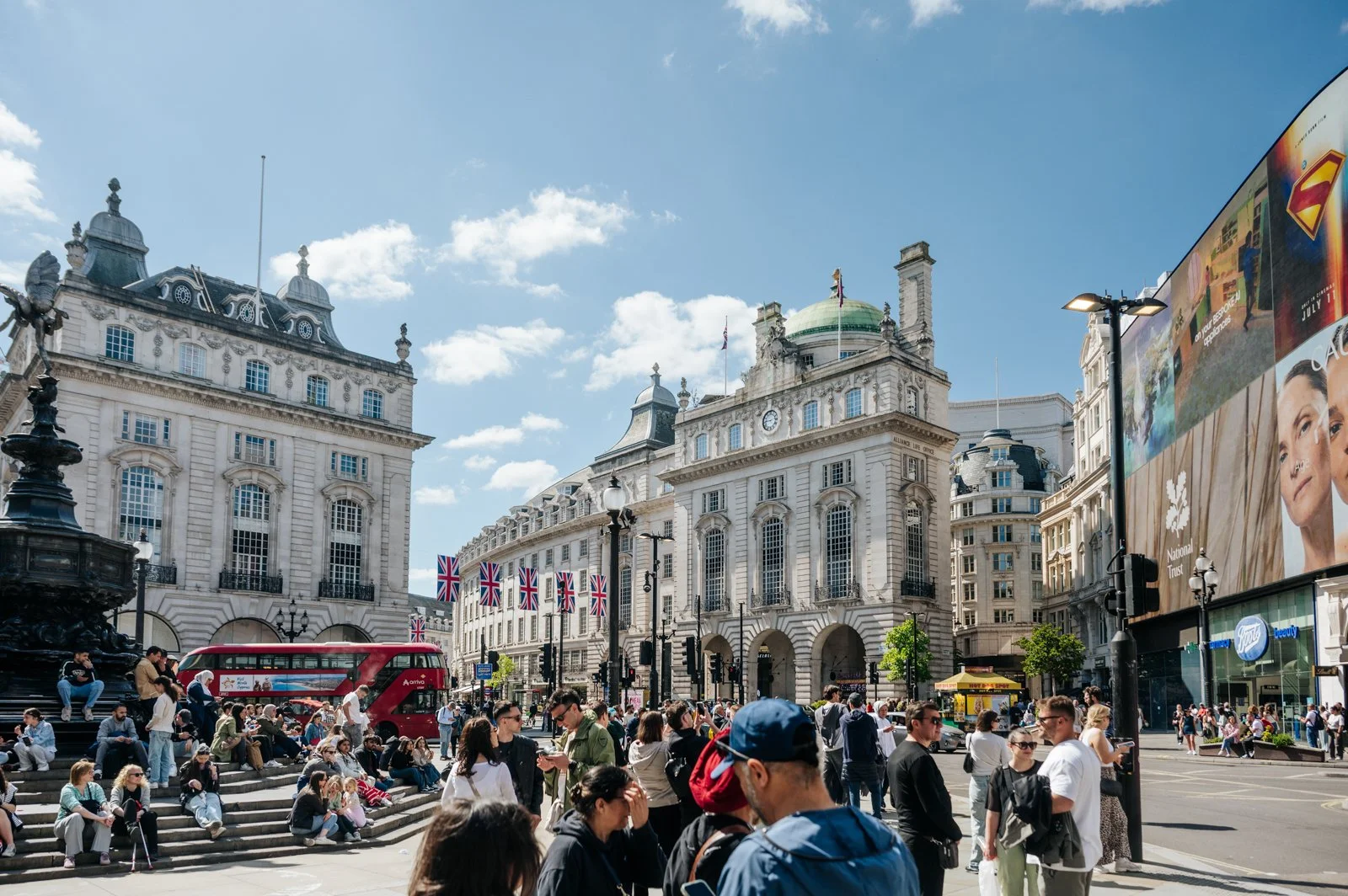 Crowd of people on a busy city street with historic buildings, Union Jack flags, and a double-decker bus in London.