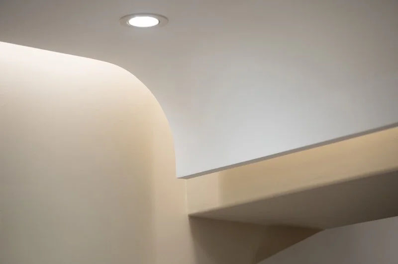 リビングの天井に施された柔らかな曲線デザイン。光が曲線に沿って反射し、木漏れ日のように降り注ぐ、視覚的な快適性を追求した空間照明。