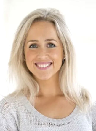 A young woman with blonde hair smiling at the camera against a plain background.