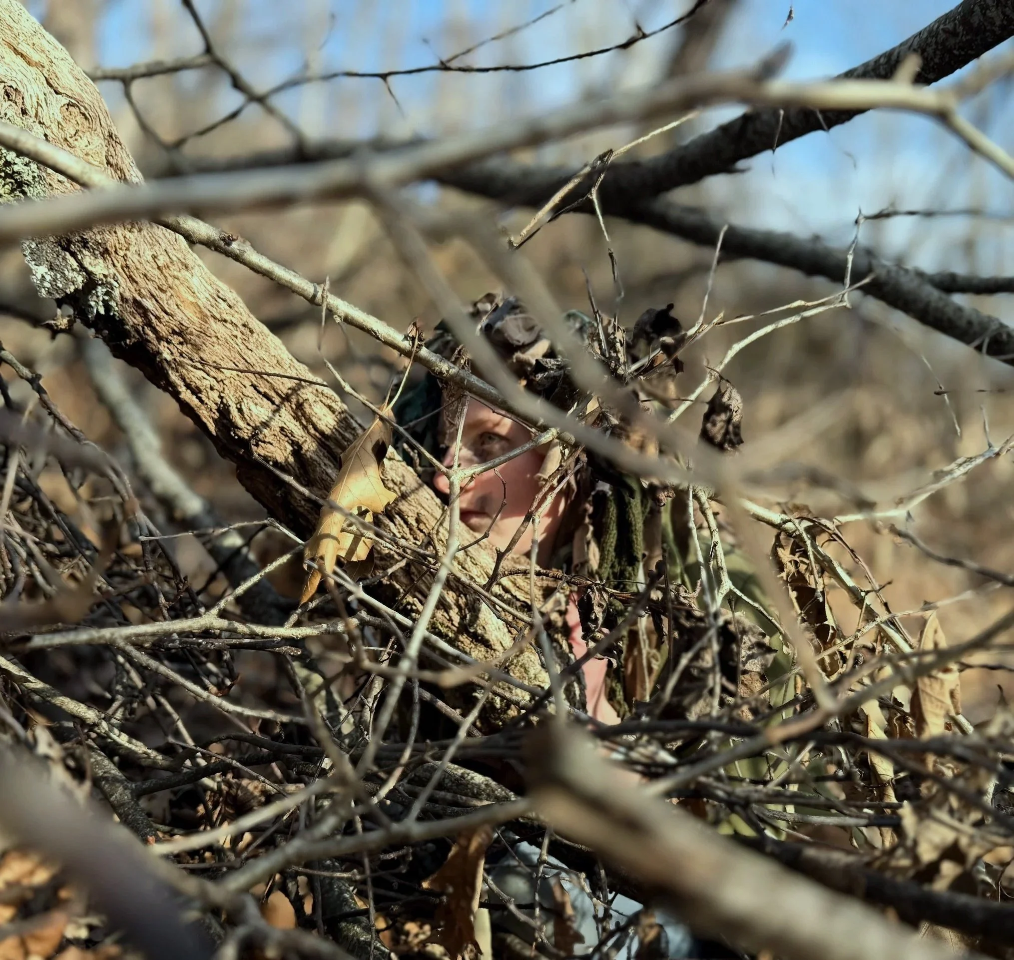 A teen dressed in camouflage sneaks in the woods during screen-free outdoor summer camp near Asheville, NC.