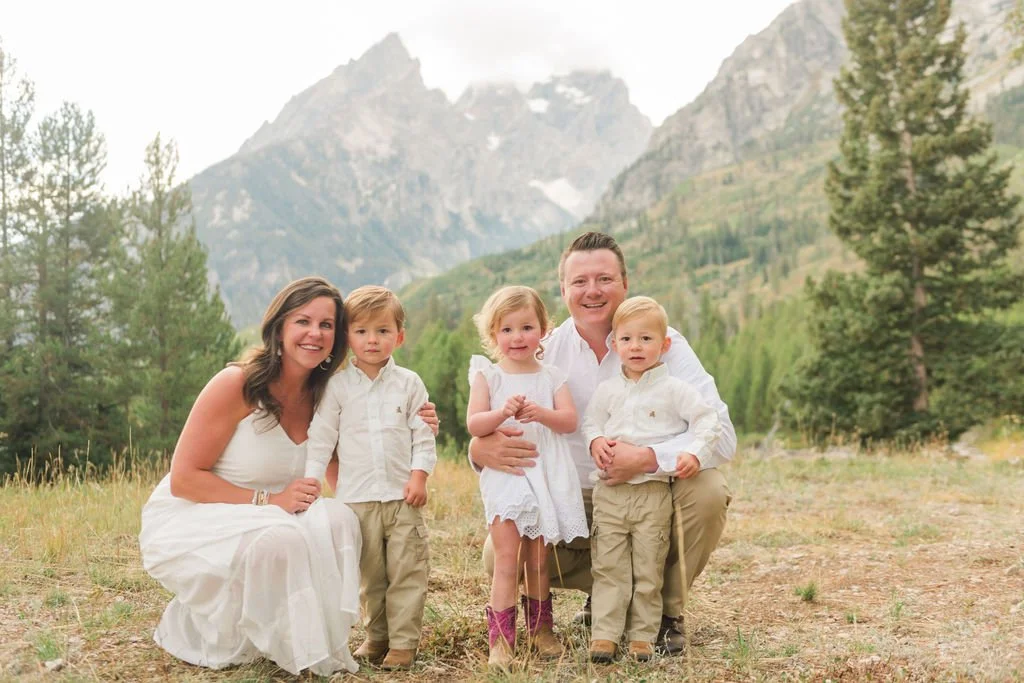 family smiling with the grand tetons behind them