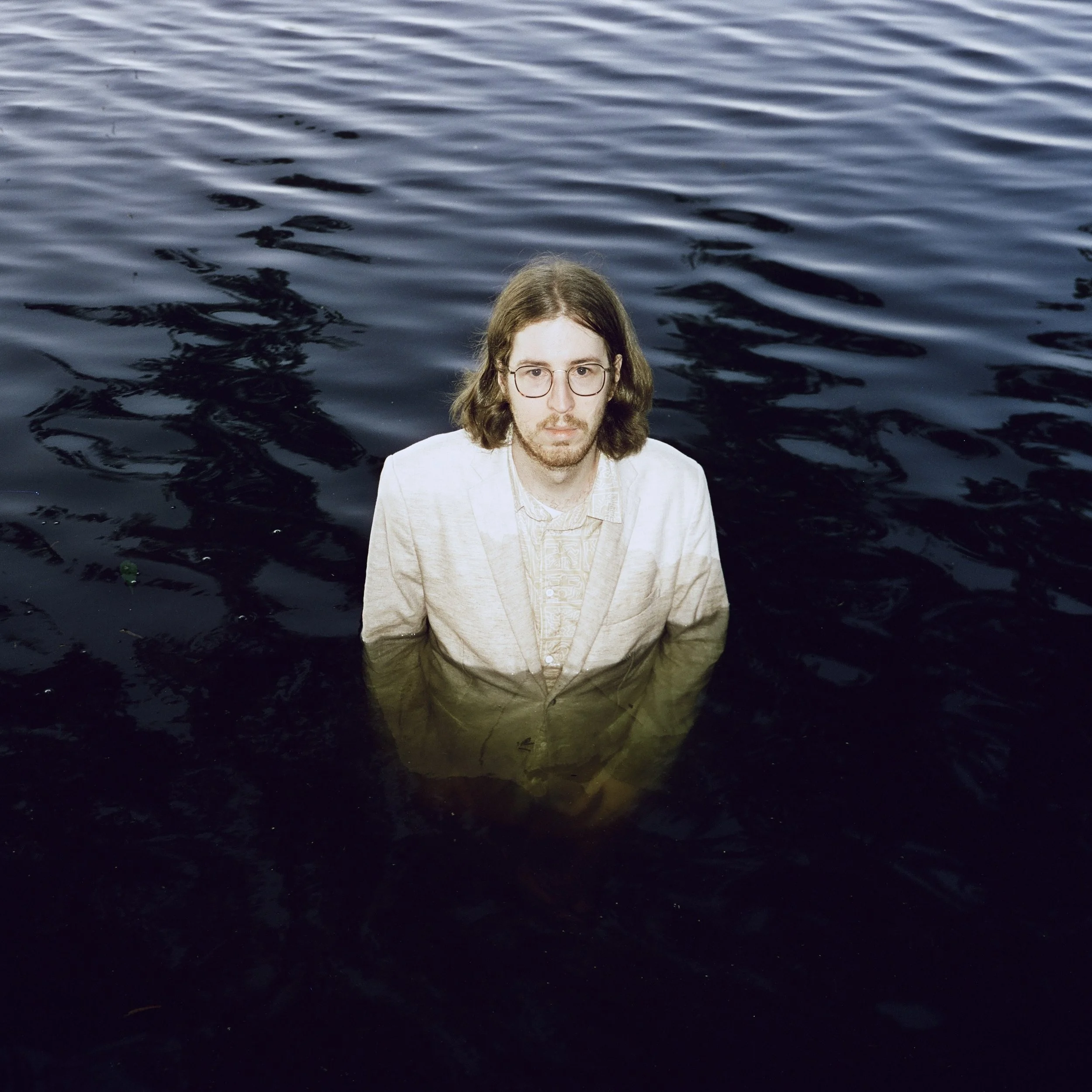 Analoges Portrait eines Mannes, der mit einem Anzug in einem See steht.