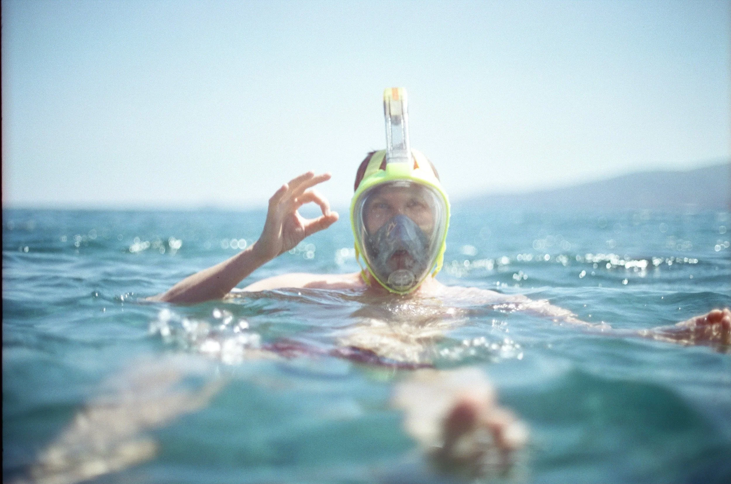 Analoges Portrait eines schnorchelnden Mannes im Meer, der das OK-Zeichen zeigt.