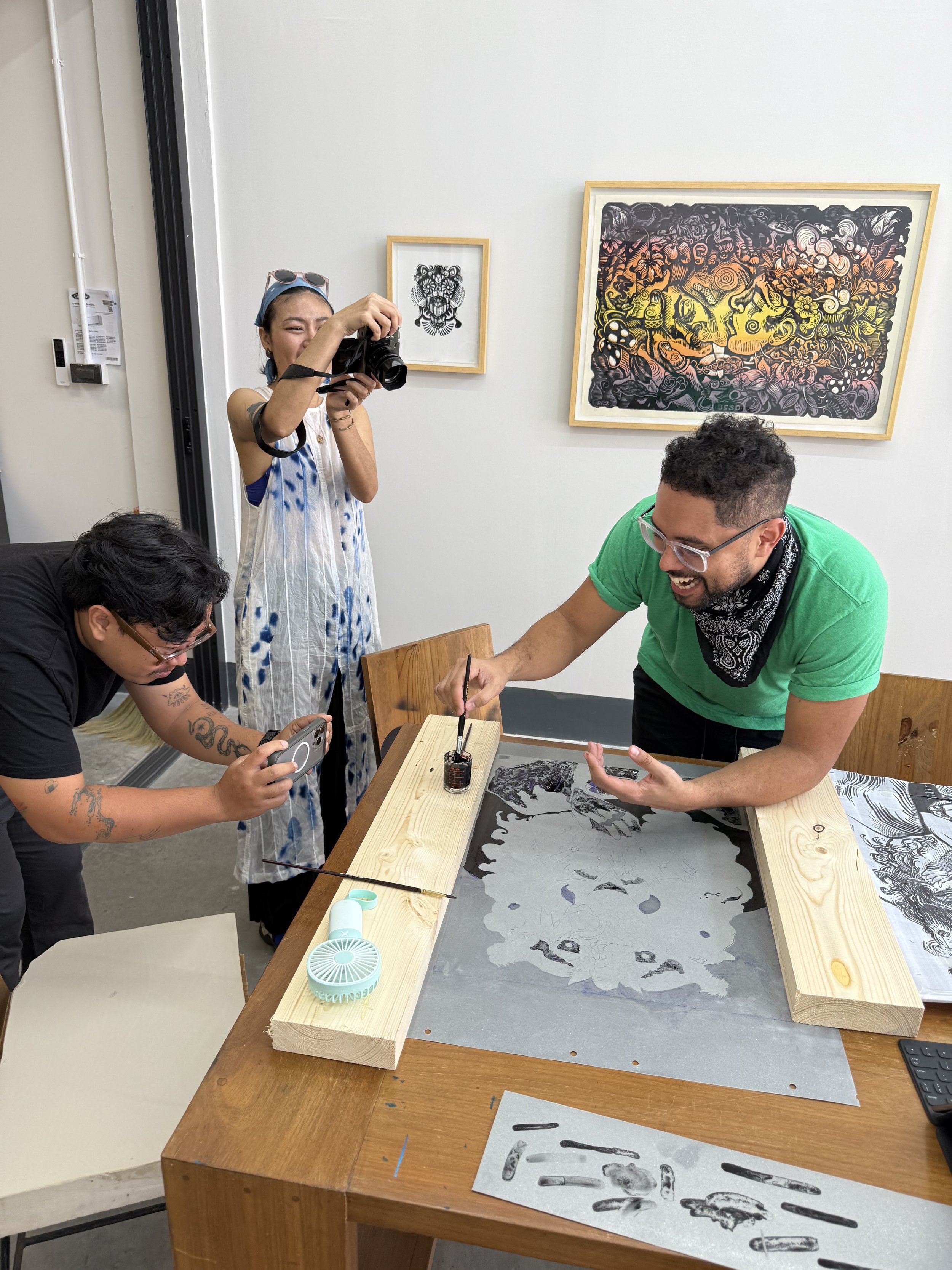 People gathered around a table observing and documenting an art piece, with artworks hanging on the wall behind them.