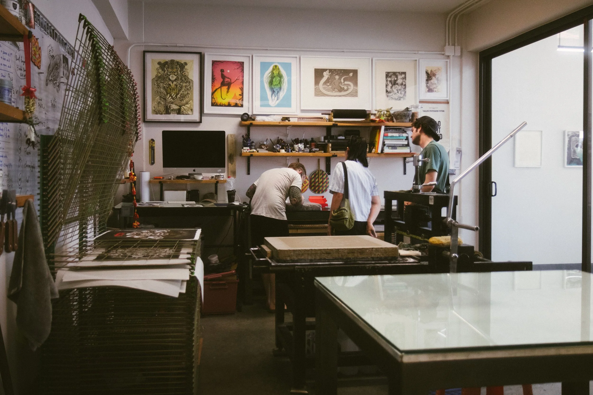 Inside an art studio with three people working, artwork on the walls, and shelves filled with art supplies.