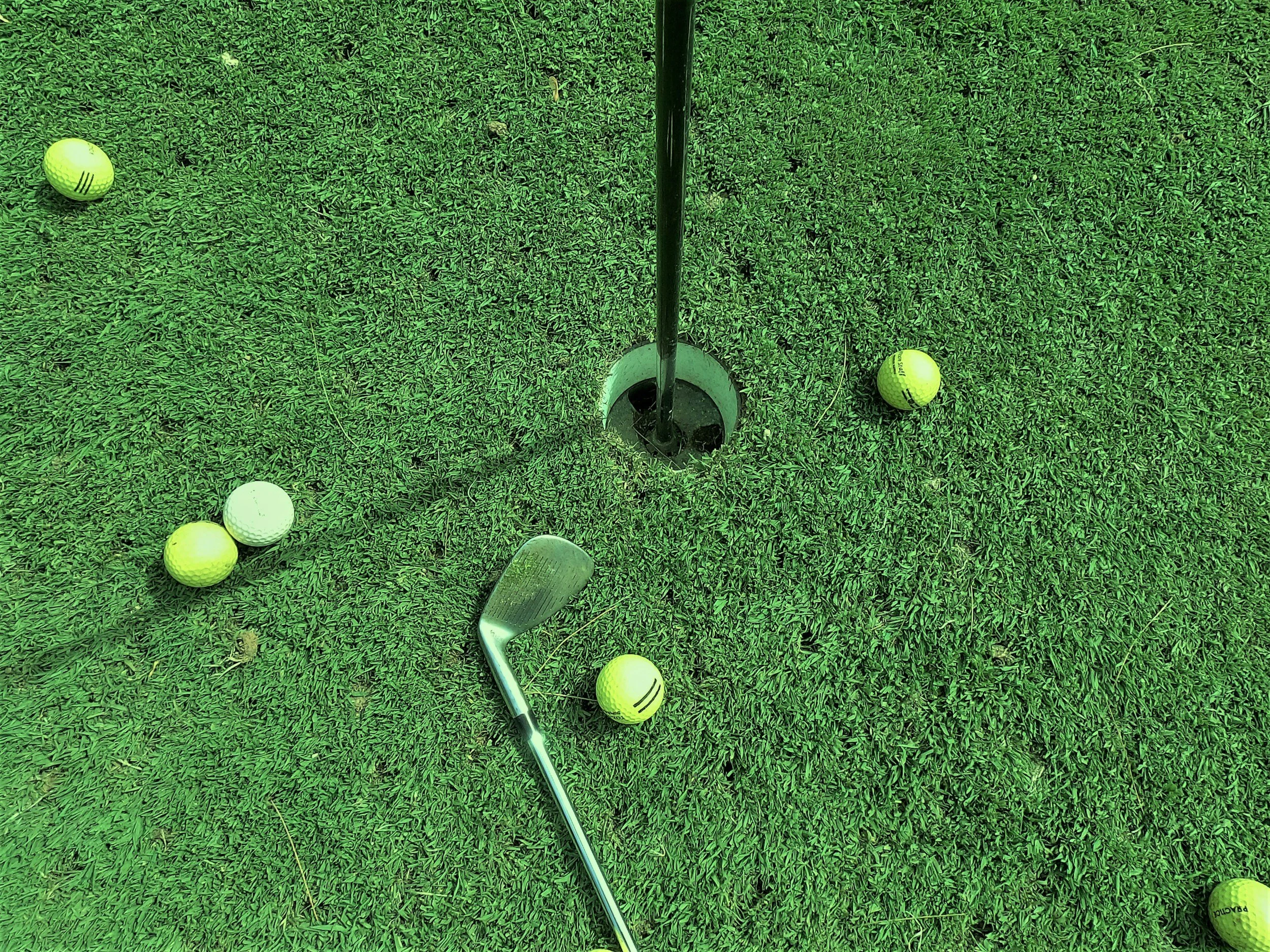 Golf course putting green with golf balls and a golf club near the hole.