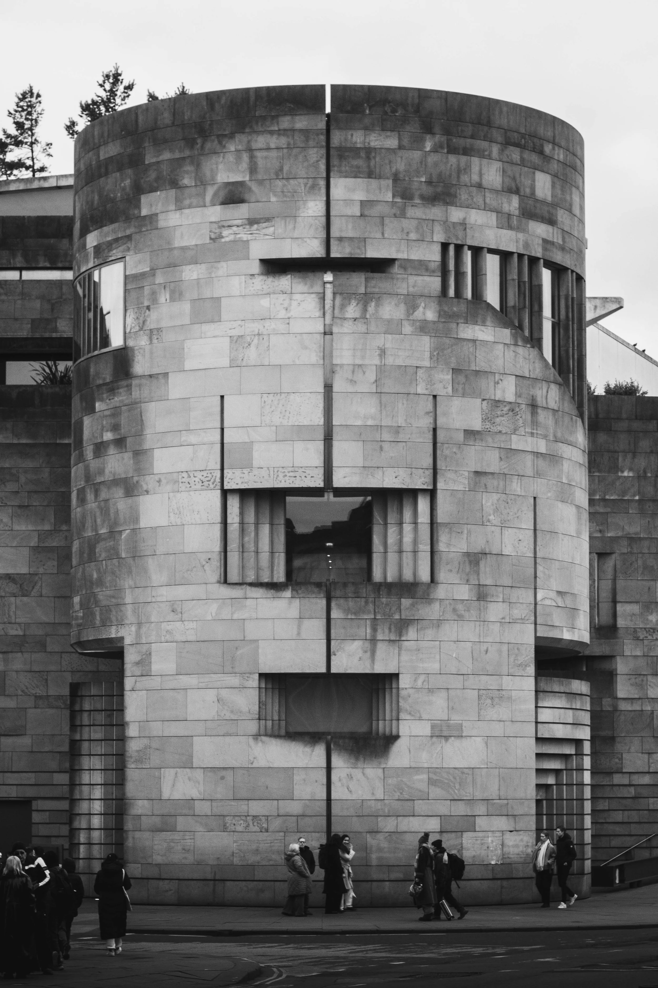 Black and white photo of a modern, circular building with people standing and walking outside.
