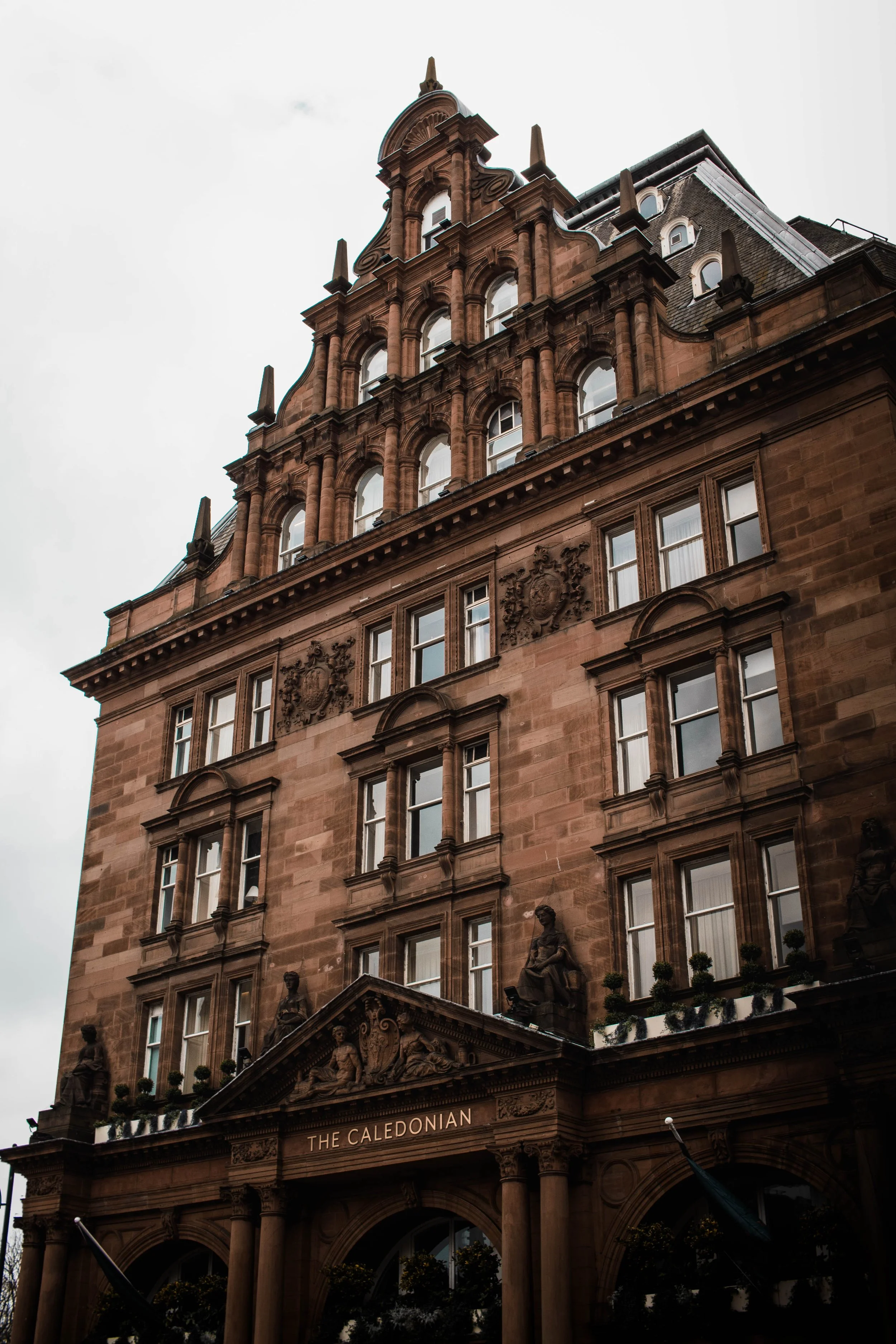 A historic multi-story building with ornate architecture, statues, and a sign that reads 'The Caledonian' at the entrance.