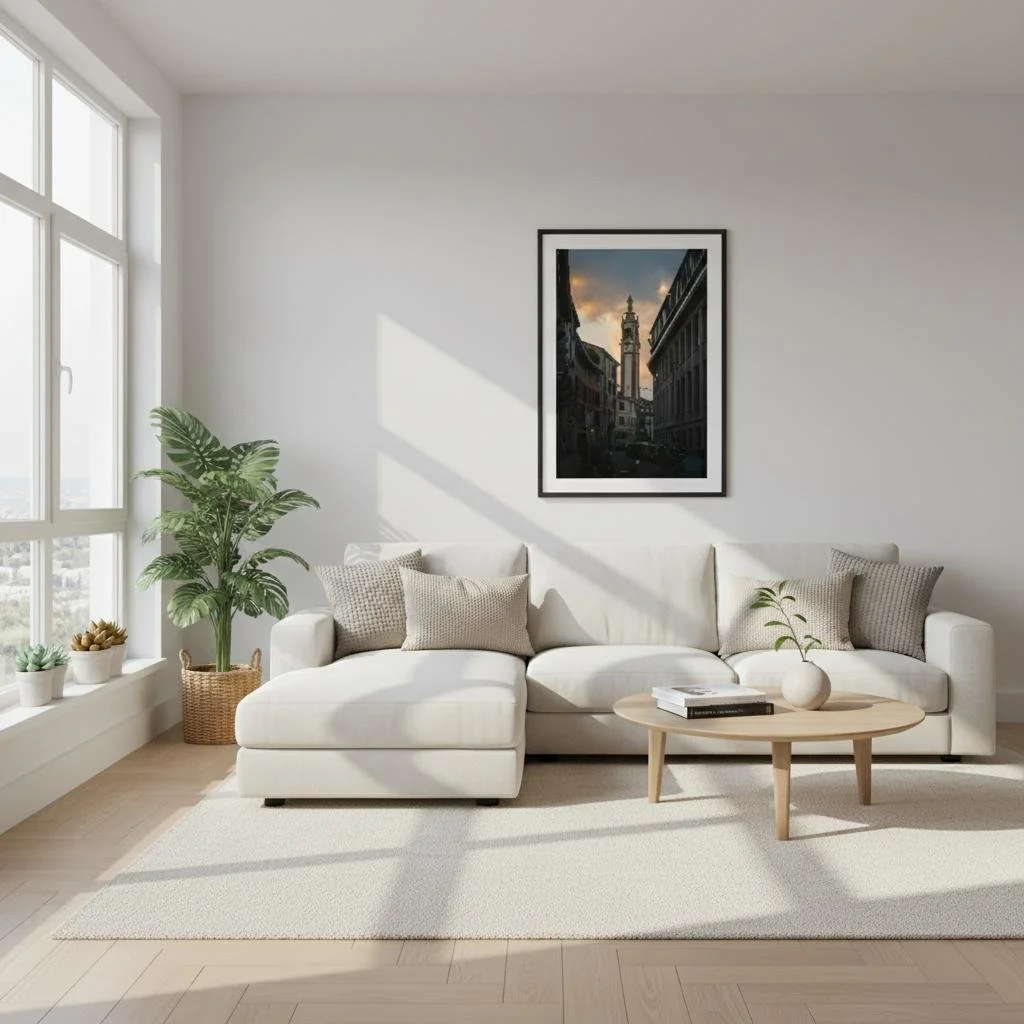 Bright living room with white sofa, beige cushions, potted plant, large window, framed cityscape artwork on white wall, light wood coffee table, and cream rug.