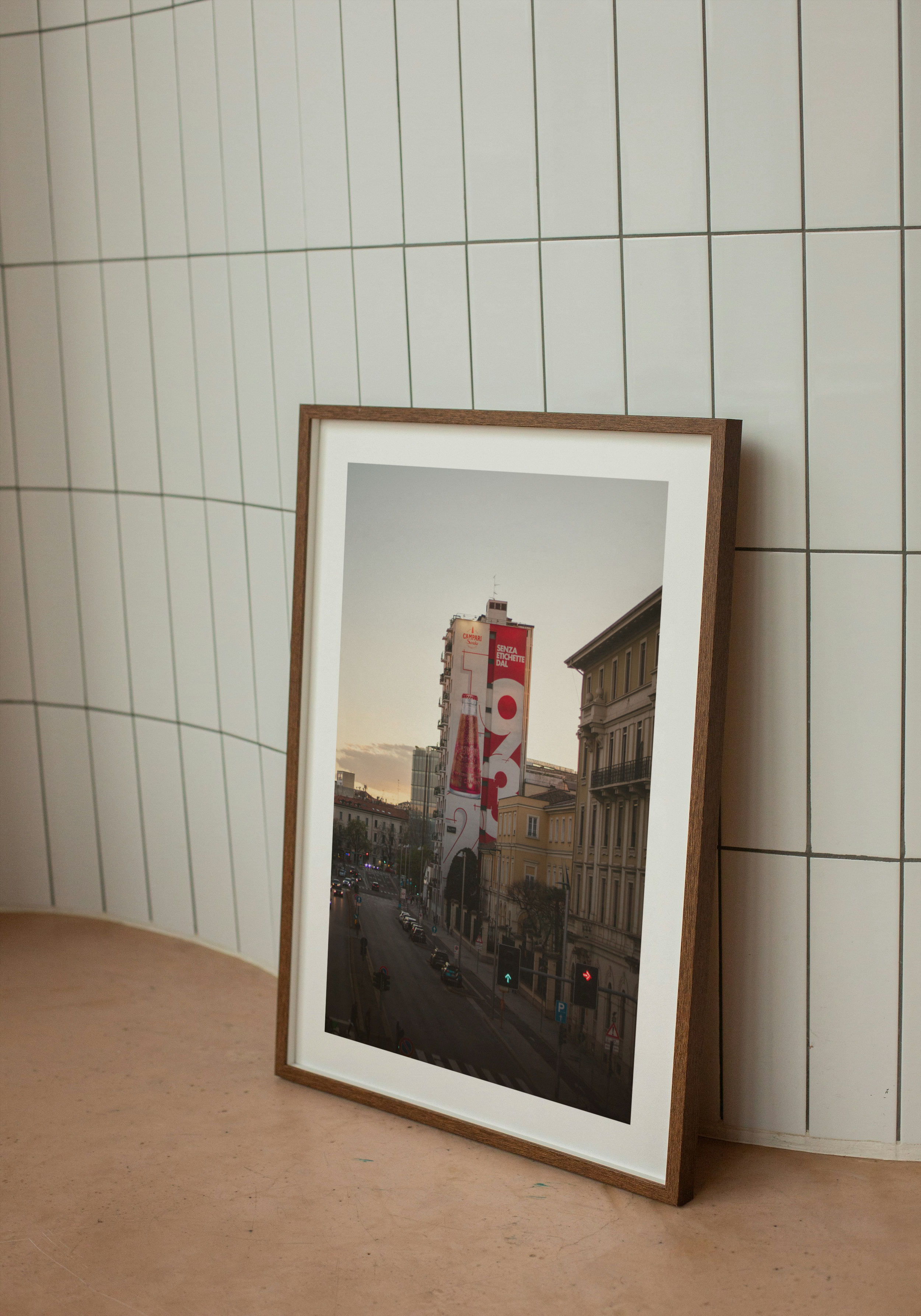 A framed photo leaning against a tiled wall. The photo shows a city street with buildings and a billboard on a tall building.