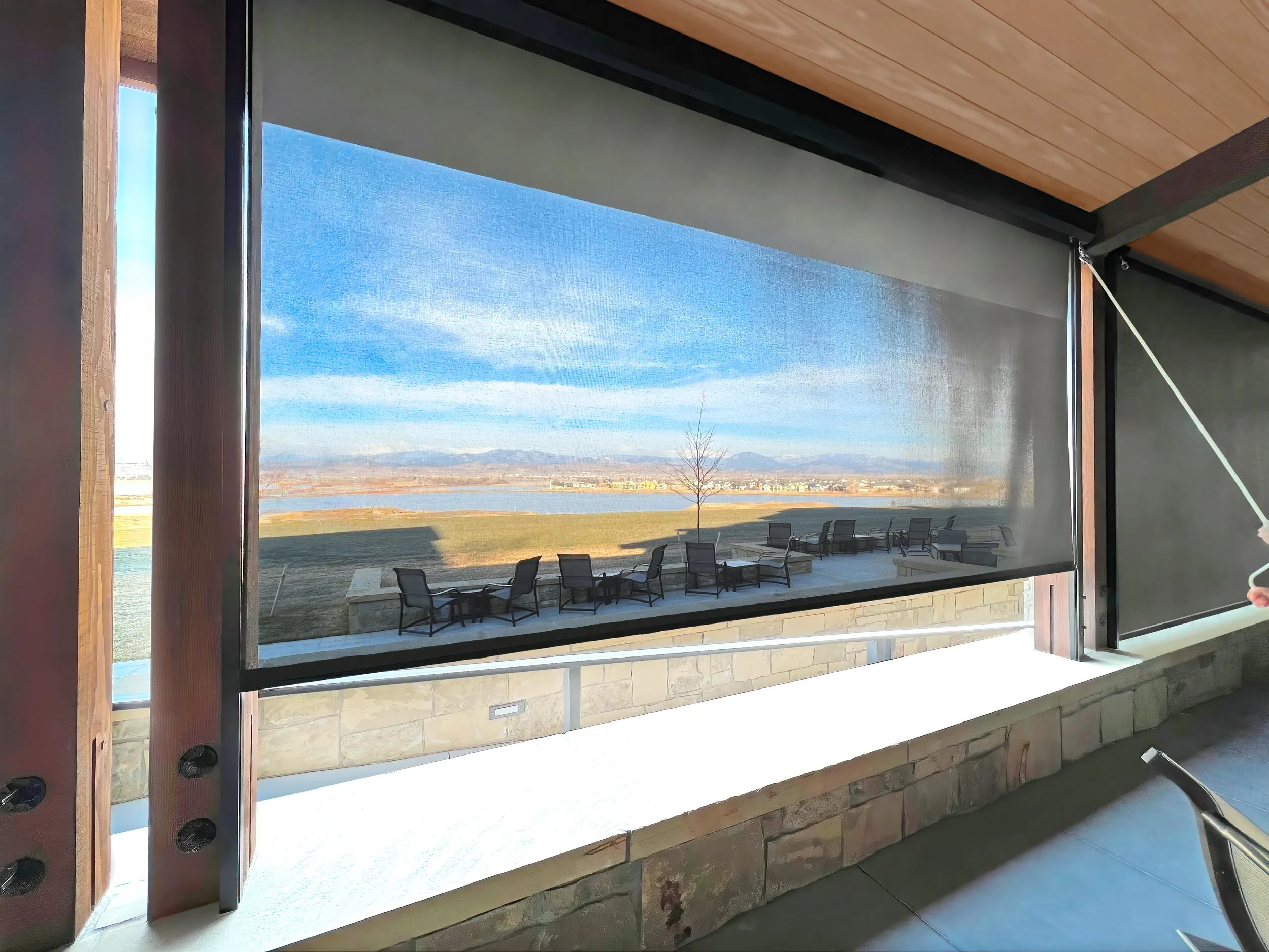 Interior view through a large window showing an outdoor landscape with a lake, trees, and mountains in the distance.