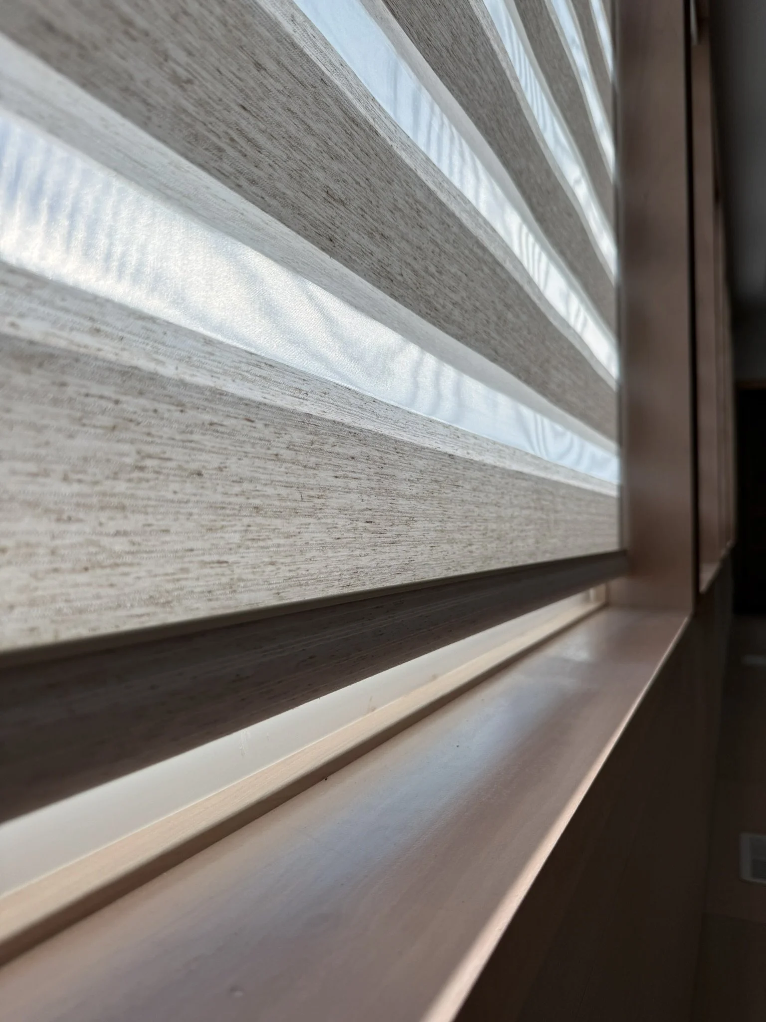Close-up of a window with horizontal wooden blinds allowing diffused sunlight to enter.