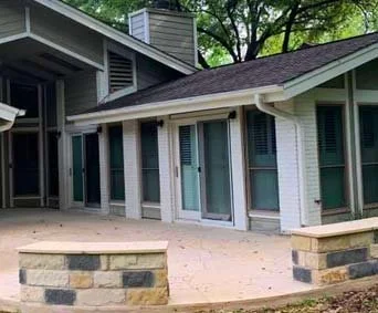 Exterior view of a house with multiple windows and a brick patio area