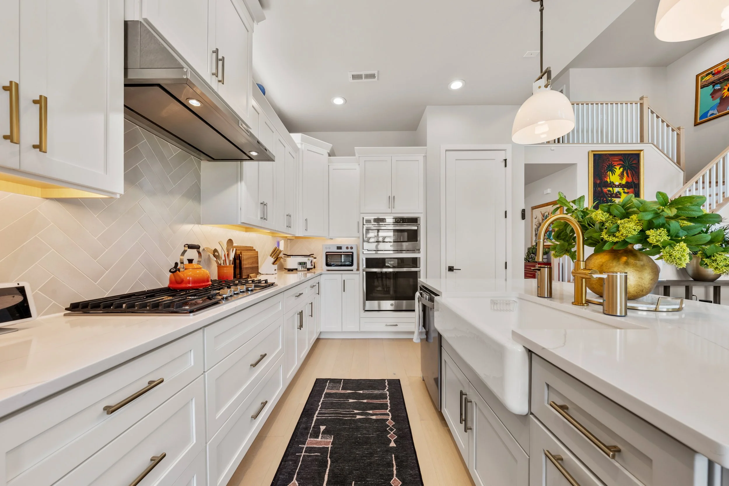Modern white kitchen with gold hardware, a black rug, and a large vase of green and yellow flowers on the countertop.