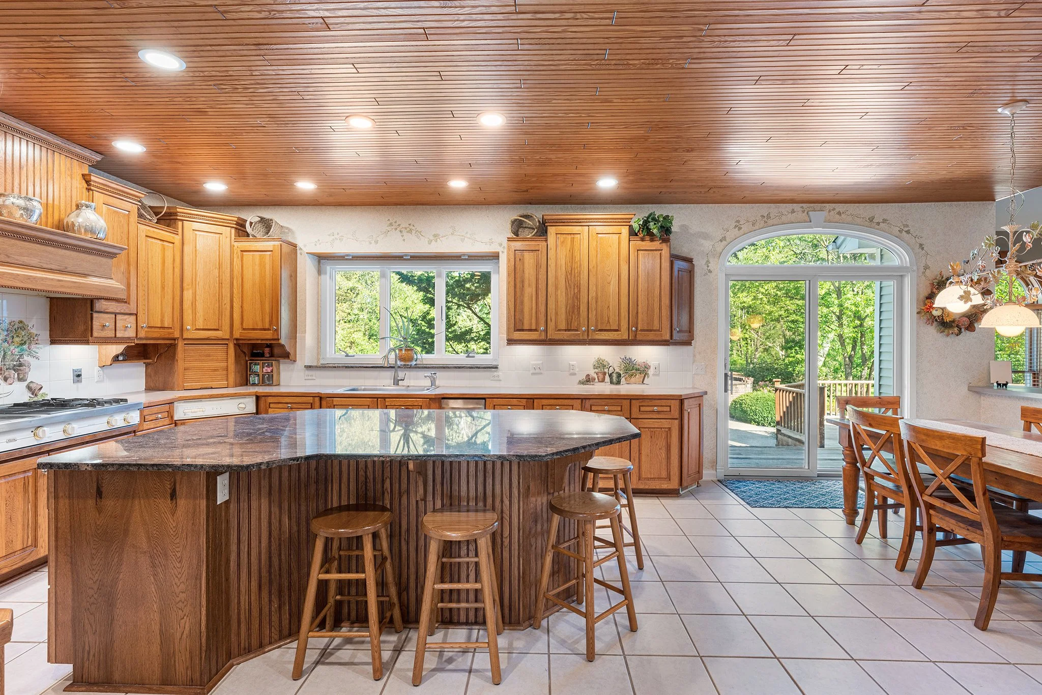 Kitchen with wooden cabinets, a granite countertop island, and a dining area with a sliding glass door leading outside, decorated in warm wood tones and natural light.
