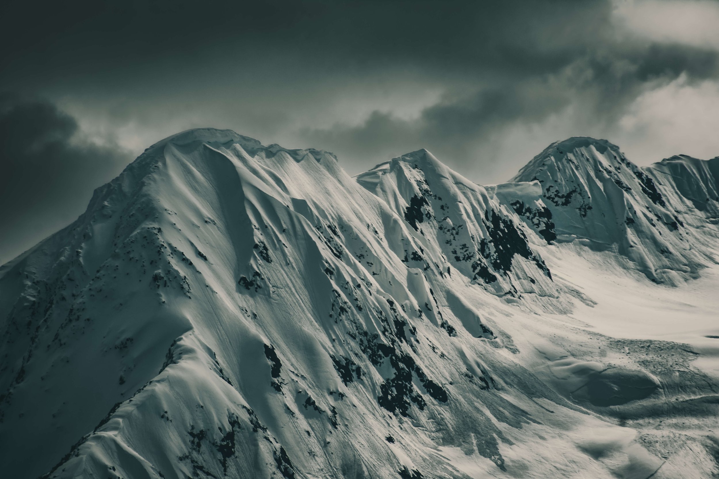 black and white photograph of snowcapped mountain peaks face, intimidating mountain range, clouds, Alaska, USA.