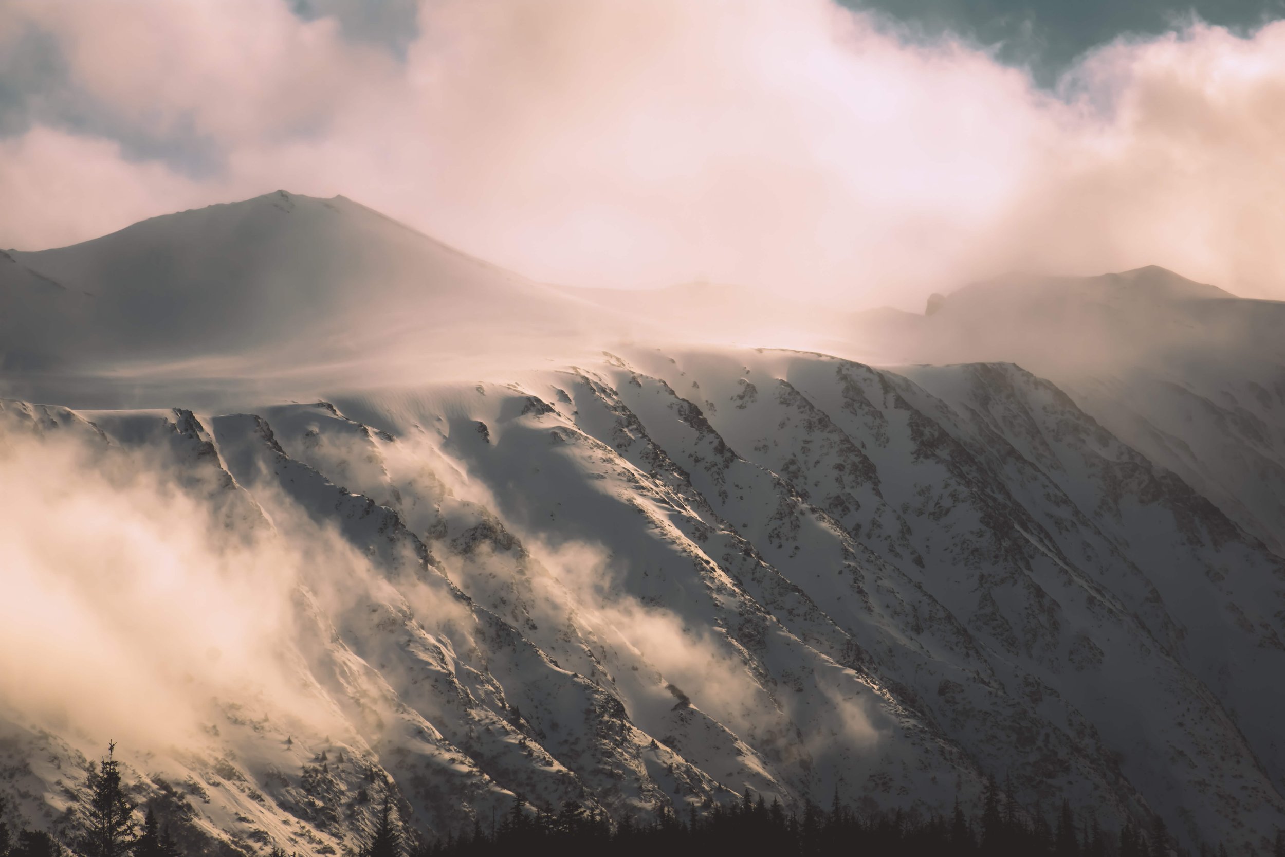 soft clouds moving over snowcapped mountain range peaks at golden hour sunset, sunrise taken in the Alsakan wilderness, Alaska, USA.