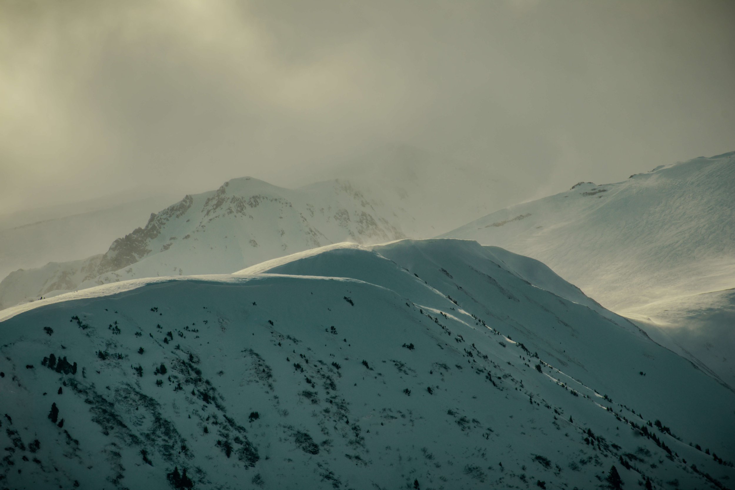 soft clouds moving over remote snowcapped mountain range peaks at golden hour sunset, sunrise taken in the Alsakan wilderness, Alaska, USA.