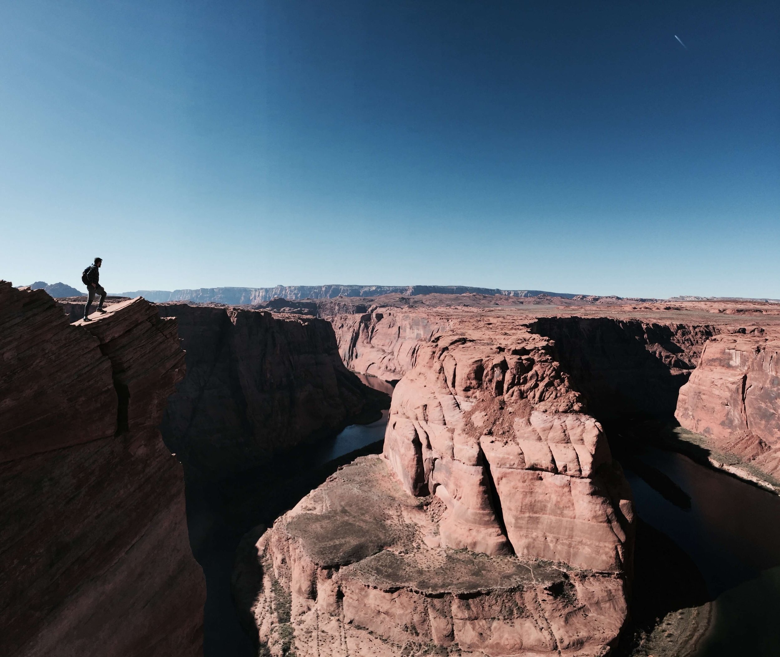 A lone man, hiker standing on desert cliff edge overlooking Horseshoe Bend, Arizona, USA, desert, Grand Canyon, Colorado River, Grand Canyon National Park, northern Arizona, desertscape, blue sky, American Southwest.