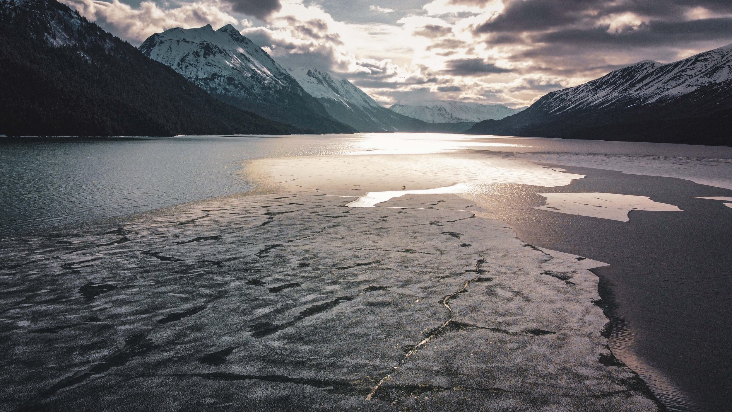 Seaward highway, a drone photograph of a remote Alaskan mountain range, snowcapped mountain peaks, mountain glaciers, frozen lake, ice, ice burgs, Alaska, USA, remote wilderness, clouds, blue sky, golden hour.