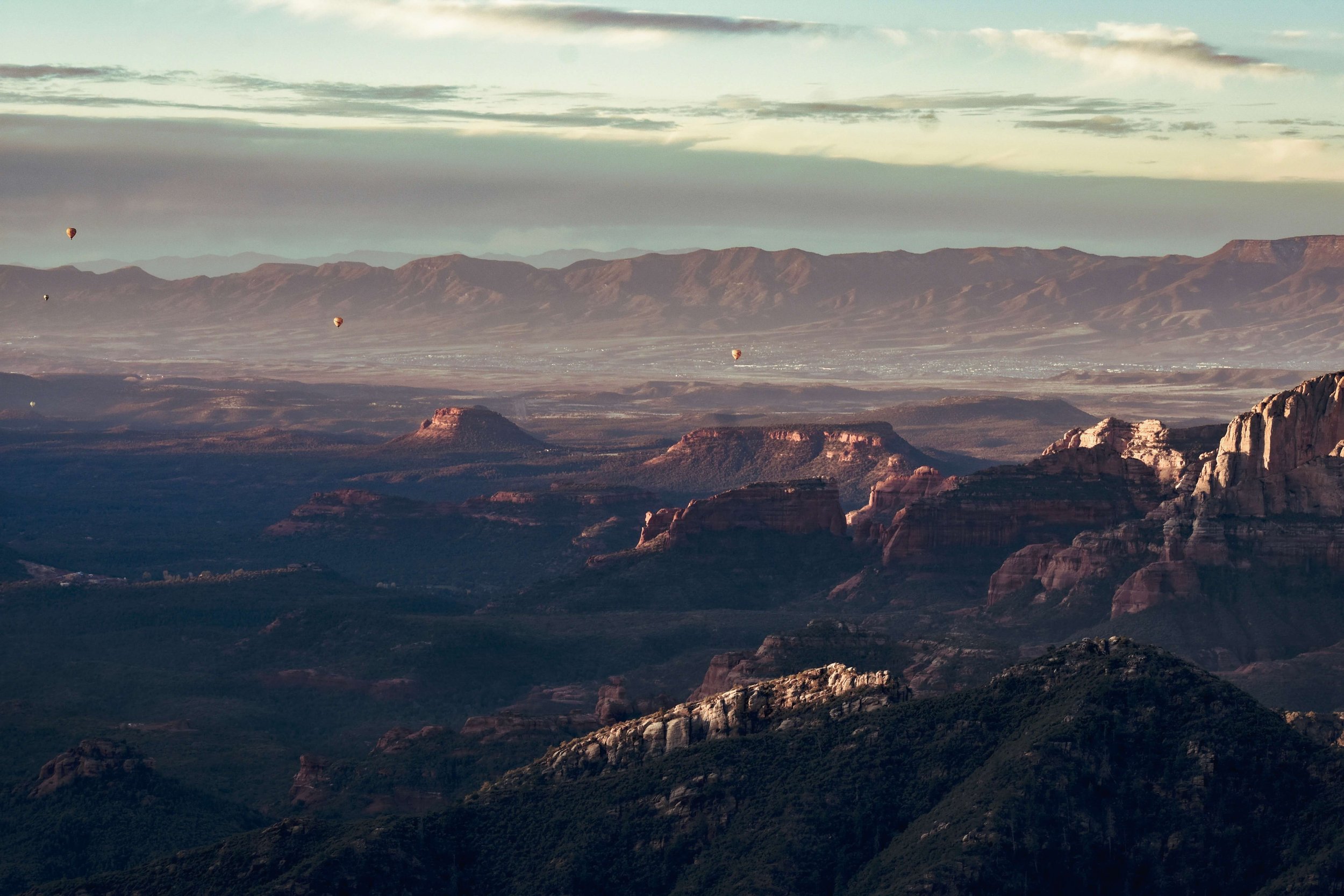 Hot air balloons take flight at sunrise as morning light rays illuminate a high desert forested canyon and the red rocks of Sedona in Northern Arizona, Arizona, USA, Edge of the World, camping, hiking, desert, cliff edge, sunset, golden hour, America