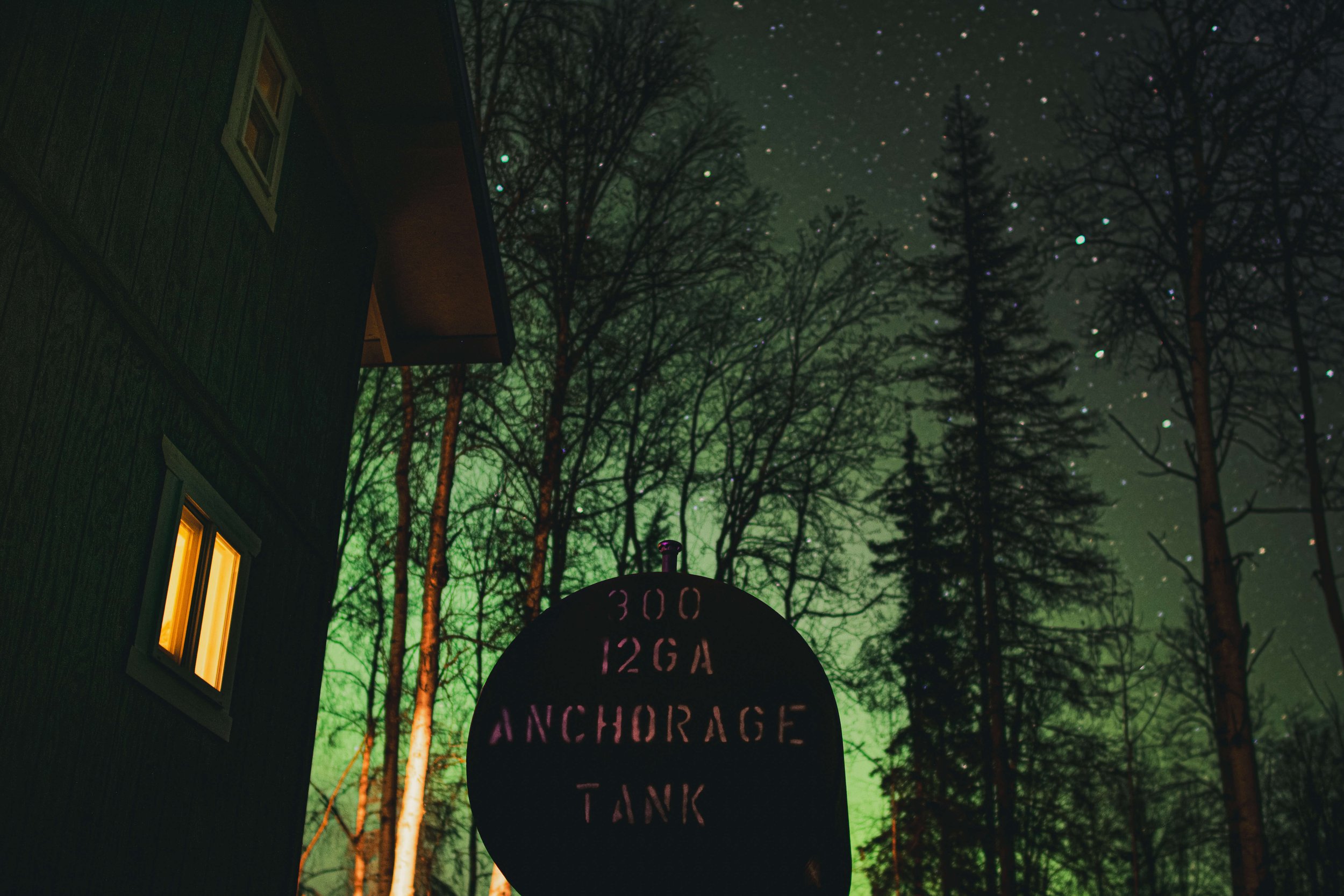 nighttime astrophotography, northern lights, green glow night sky, Alaska, USA, Anchorage water tank, green cabin, Air Bnb, AirBnb, stars, rising pines, forest.