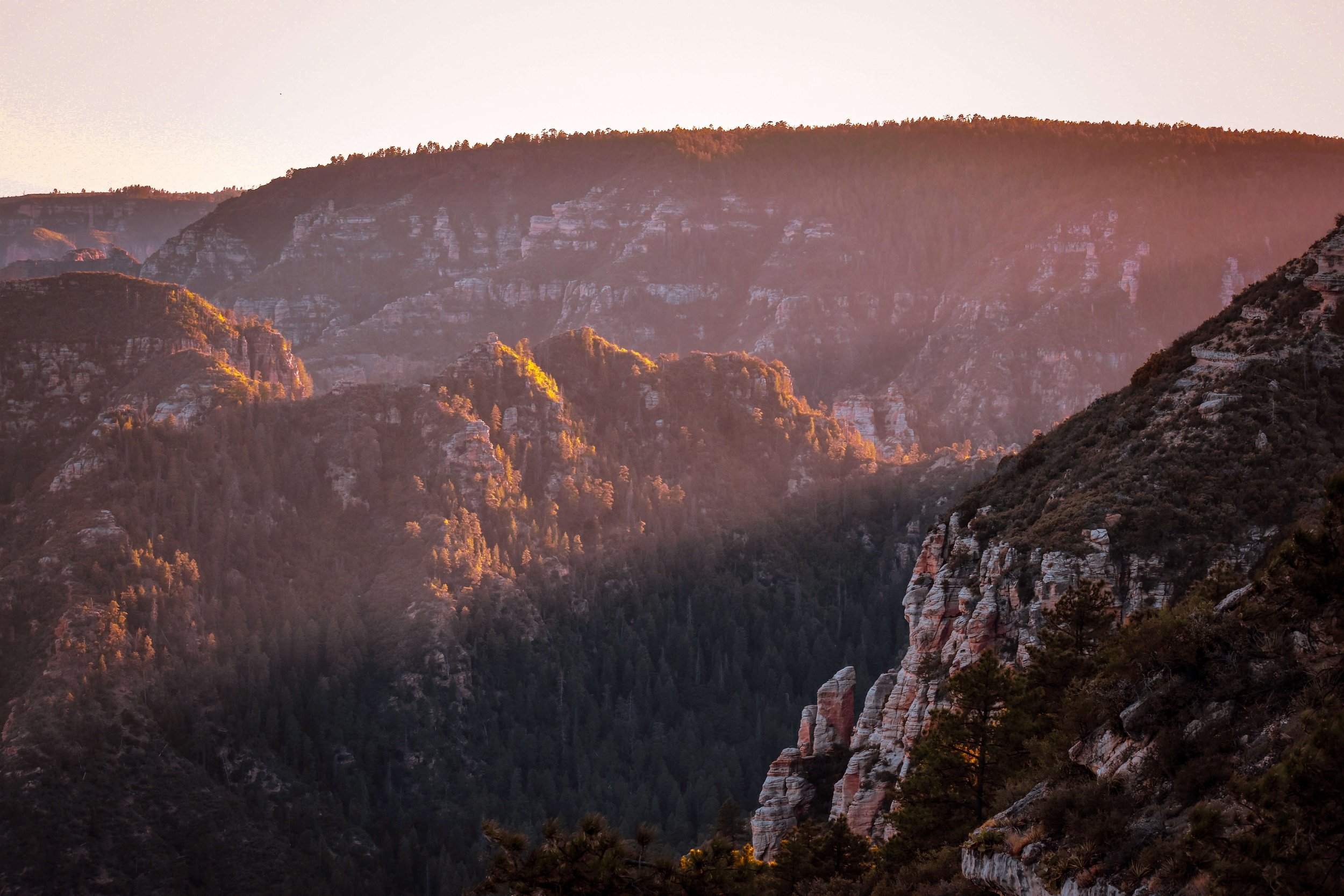 Sunset light rays illuminate a high desert forested canyon in Northern Arizona, Sedona, Arizona, USA, red rocks, Edge of the World, camping, hiking, desert, cliff edge, sunrise, golden hour, American Southwest.