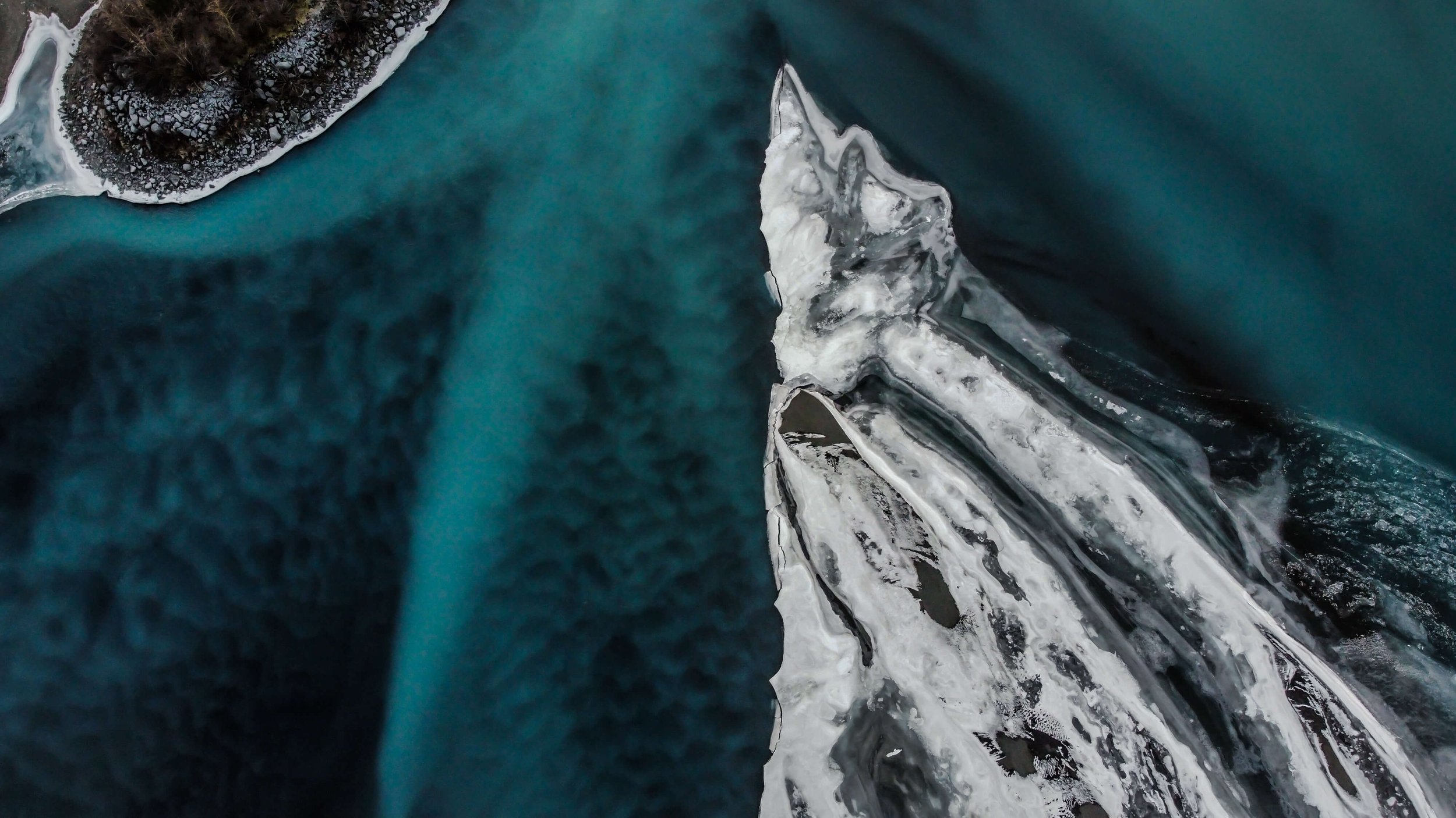 a drone photograph taken from the air of a frozen winding river in Alaska wilderness, abstract nature photography, glacial blue, white ice, black sand and sediments, Alaska, USA.