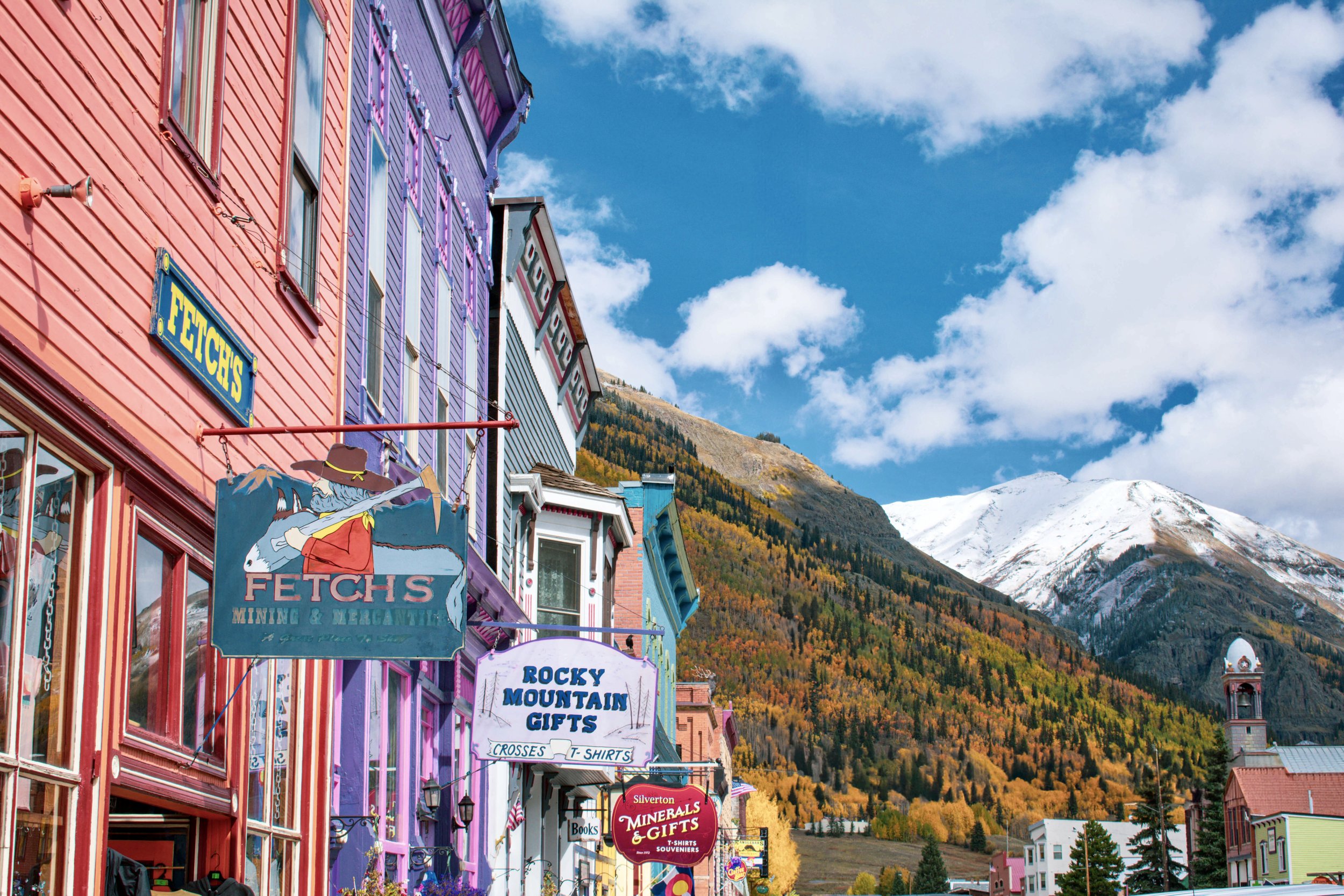 The colorful streets of main street downtown Silverton, Colorado, a mountainside forest of aspen trees in autumn colors of yellow, gold, orange, red, and green, along with snowcapped mountain peaks in the background, autumn, fall foliage, USA, Rocky