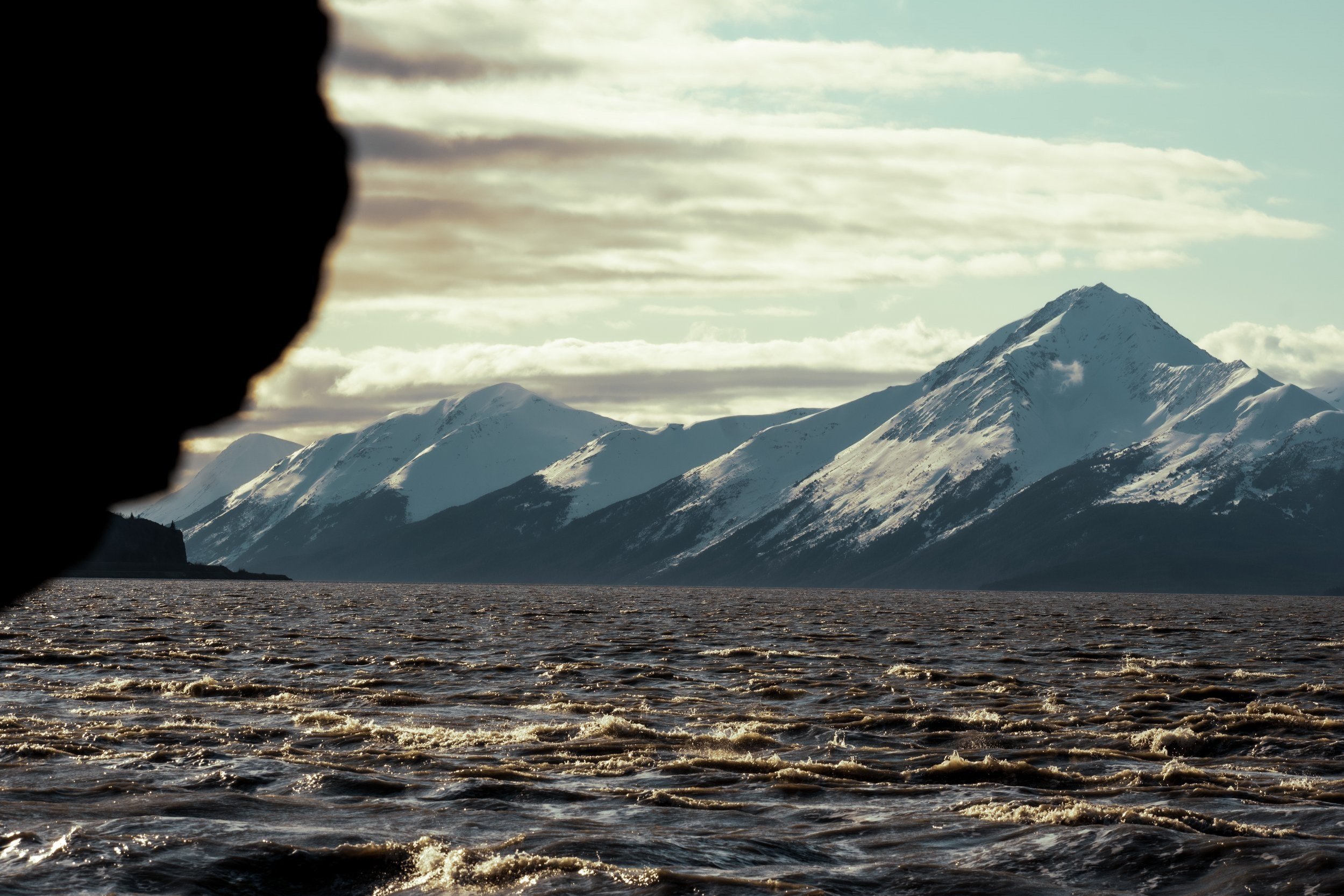 Seaward highway, zoomed in photograph of a remote Alaskan mountain range, snowcapped mountain peaks, mountain glaciers, Alaska, USA, rough seas and open water in foreground.
