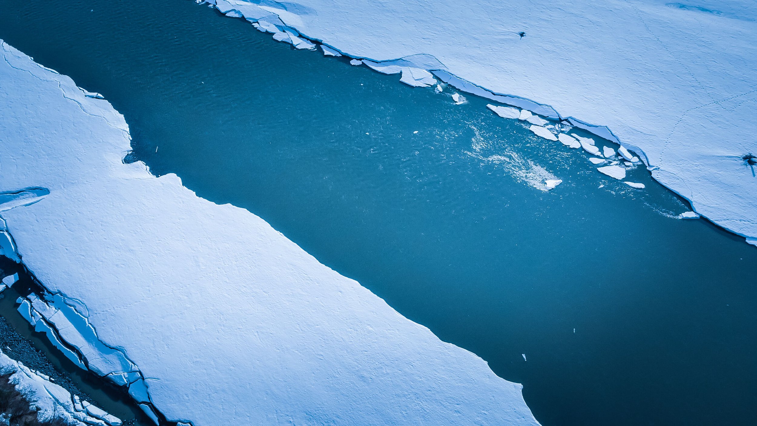 a drone photograph taken from the air of a frozen river in Alaska wilderness, abstract nature photography, glacial blue, white ice, iceberg, animal tracks, Alaska, USA.