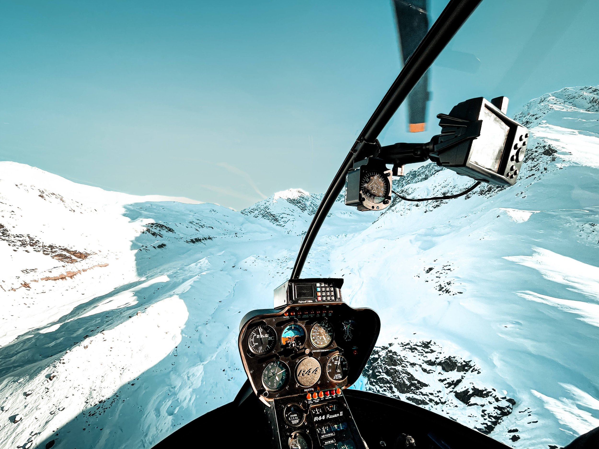 cockpit of a helicopter flying over a remote Alaskan mountain range photographed from above, snowcapped mountain peaks, blue sky, helicopter instrumentation, Alaska, USA, helicopter tour.