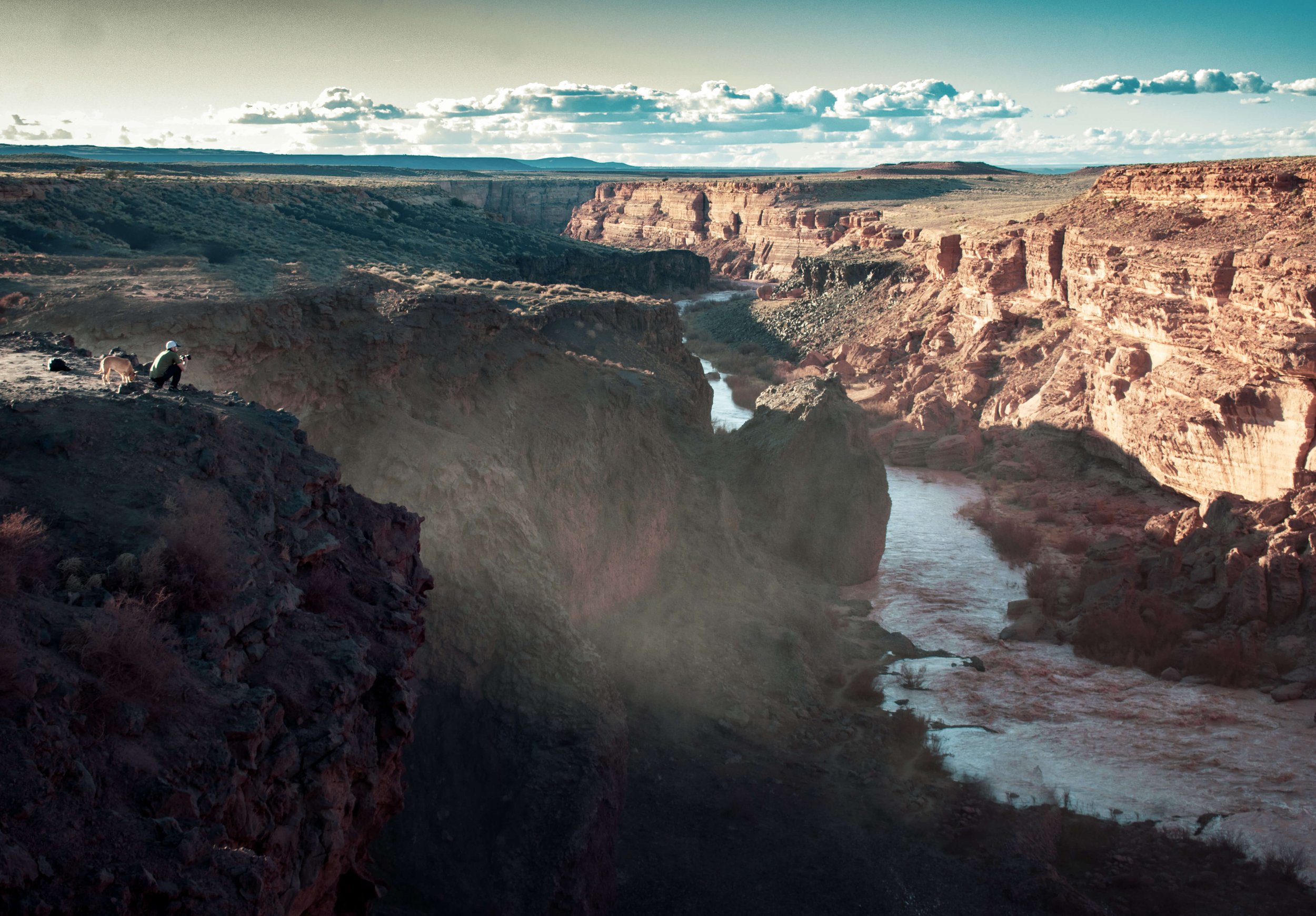 A lone man, photographer and his dog on a desert cliff edge overlooking Grand Falls, Arizona, USA, desert, monsoon, monsoon rains, northern Arizona, chocolate waterfall, mud flow, sunlight mist, desertscape, blue sky, clouds, sun rays, American South