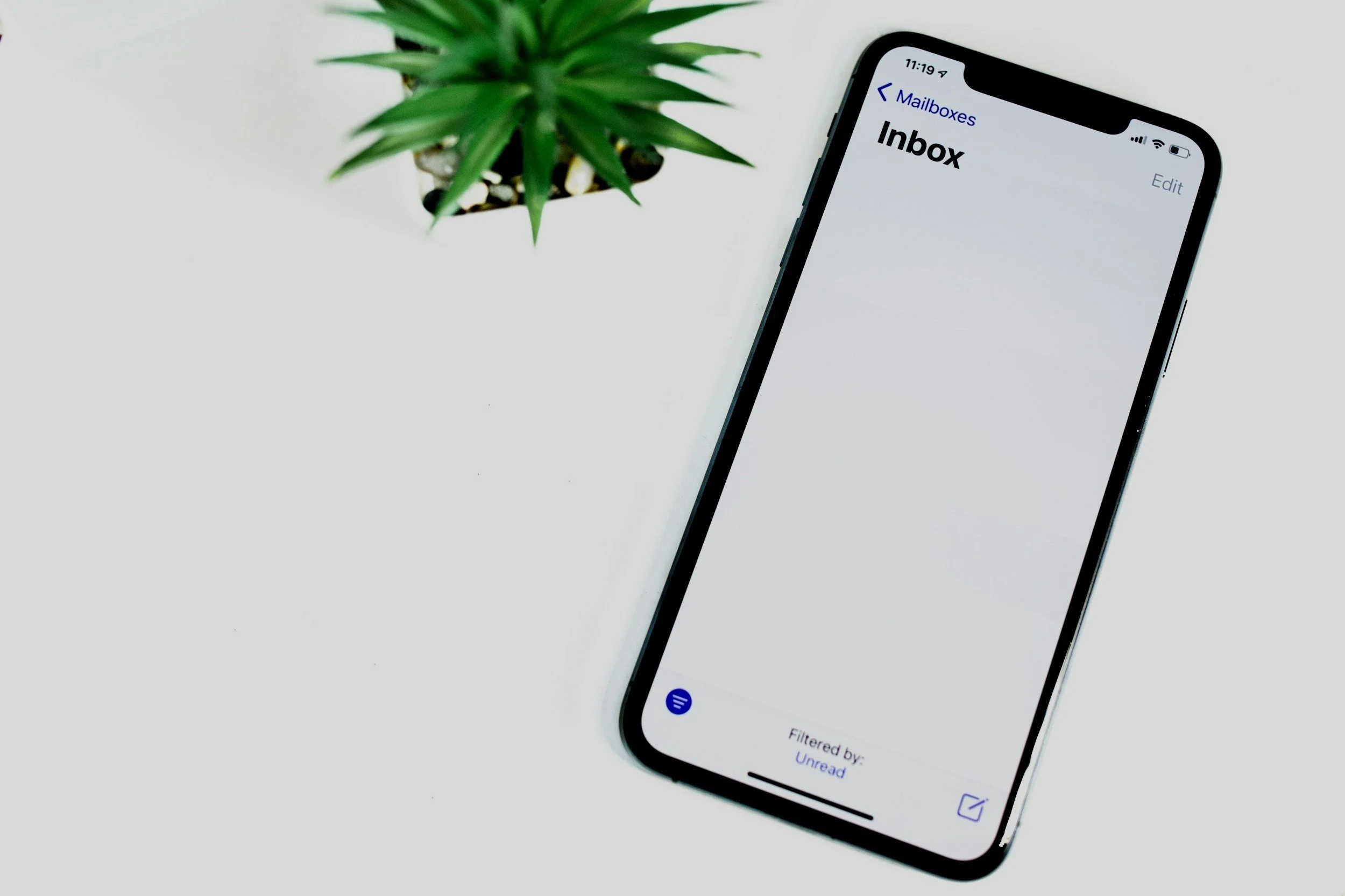 An iPhone displays an empty inbox on a white surface next to a green potted succulent plant.