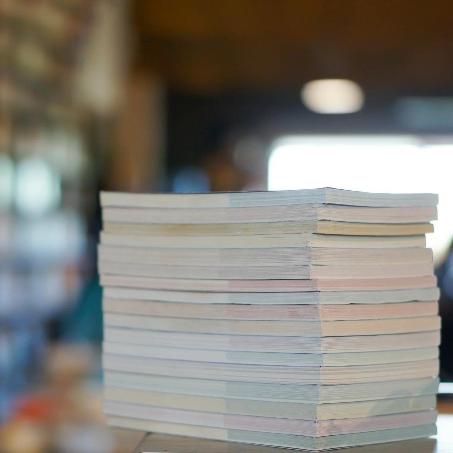Stack of books or magazines on a table inside a room with blurred background.