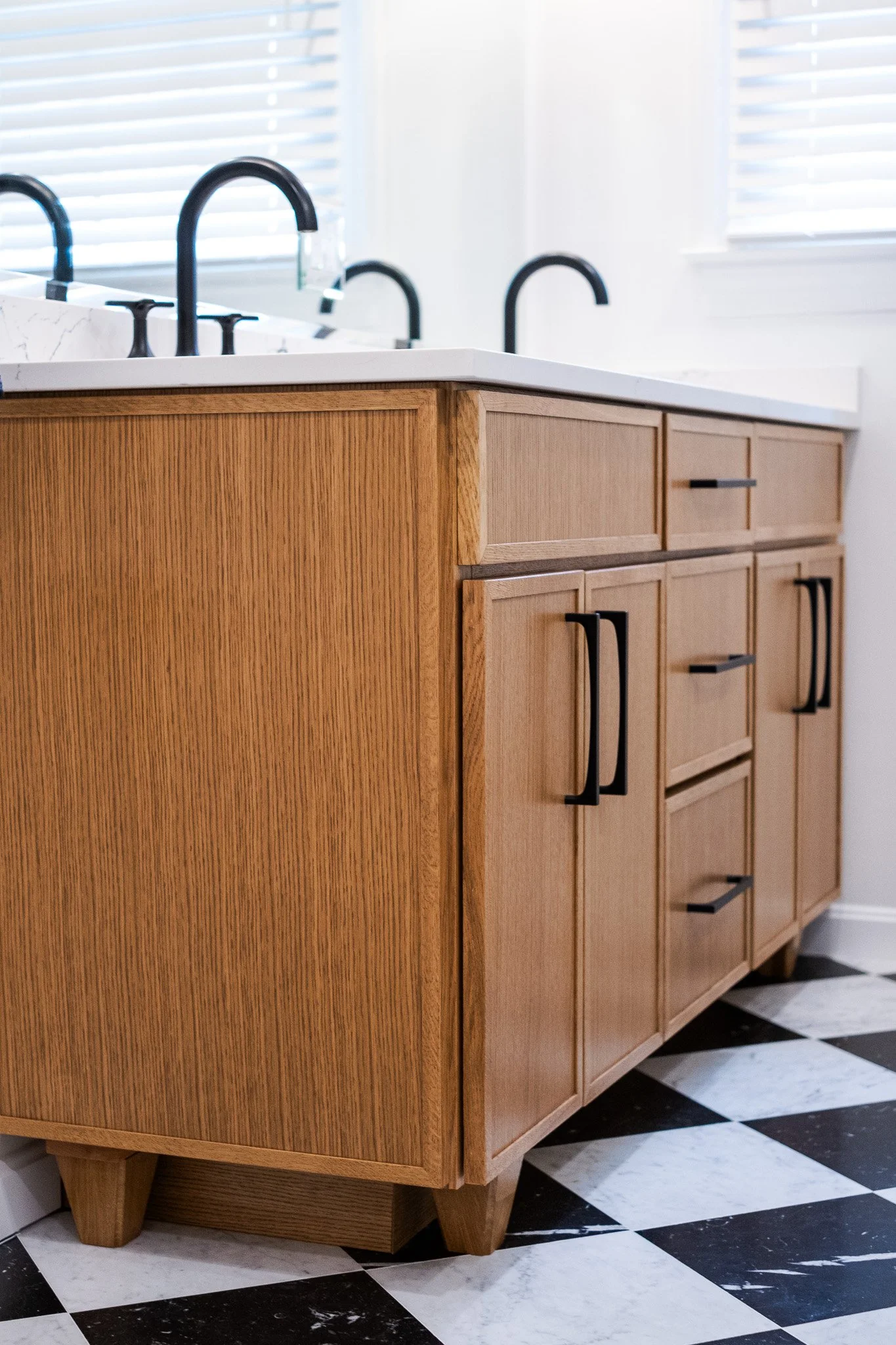 Kitchen cabinet with black handles, white countertop, black faucets, and checkered black and white floor.