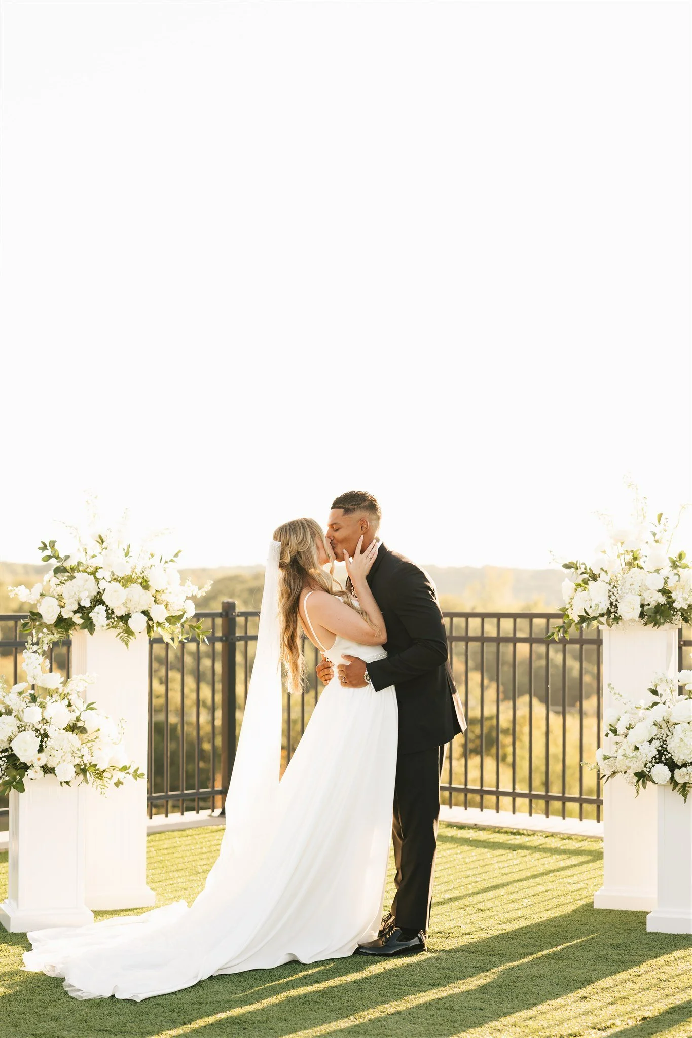 Bride and Groom sharing their first kiss at the alter with white florals and overlooking ceremony site
