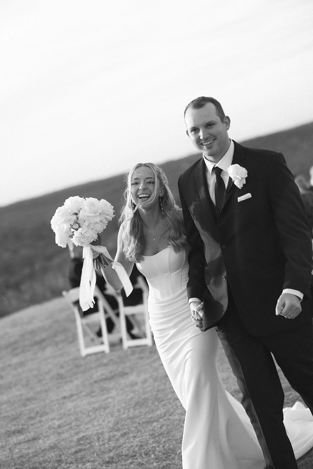 black and white photo of bride and groom holding one another as they are exiting their ceremony.