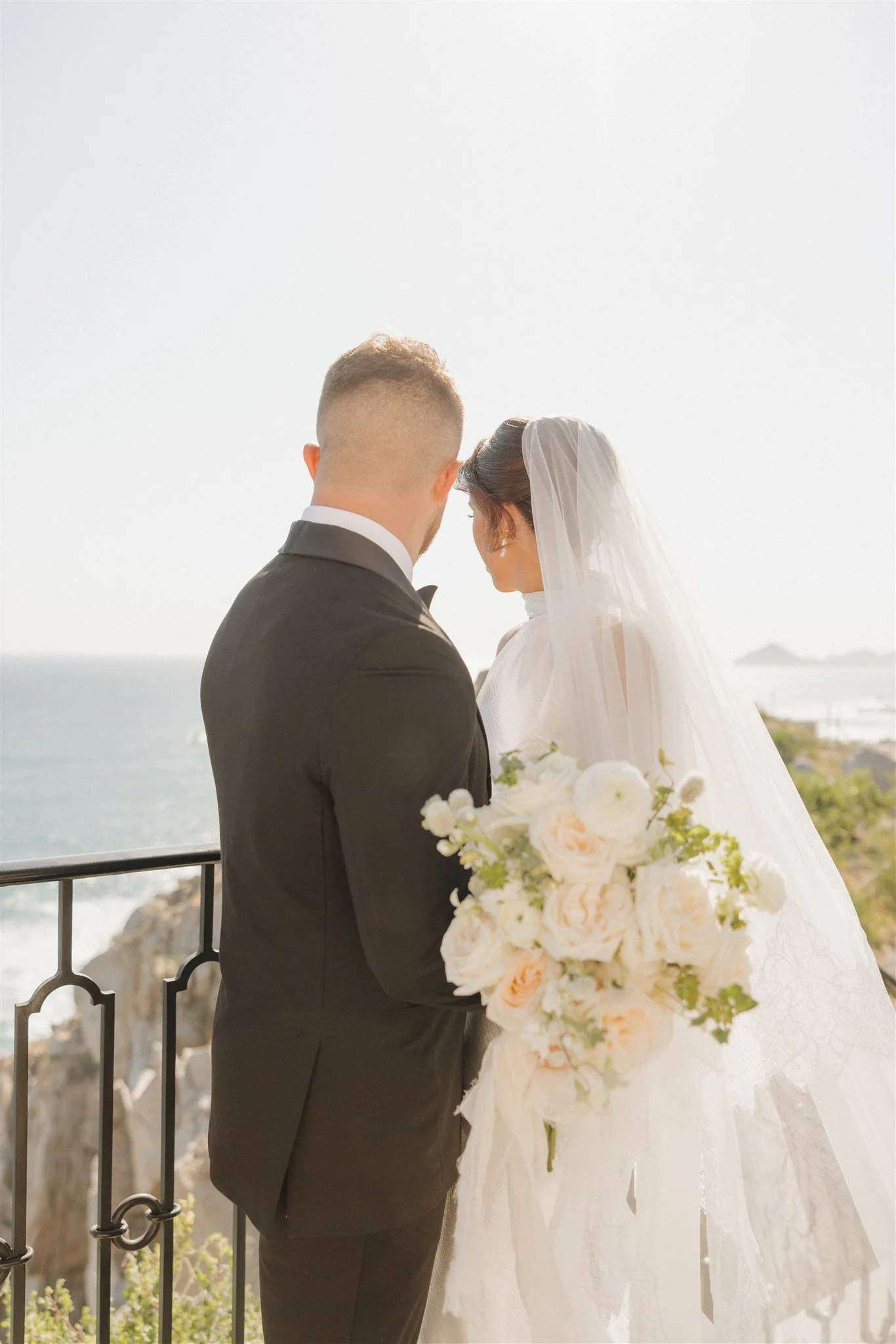 bride and groom overlooking beach side reception at their destination wedding with white florals