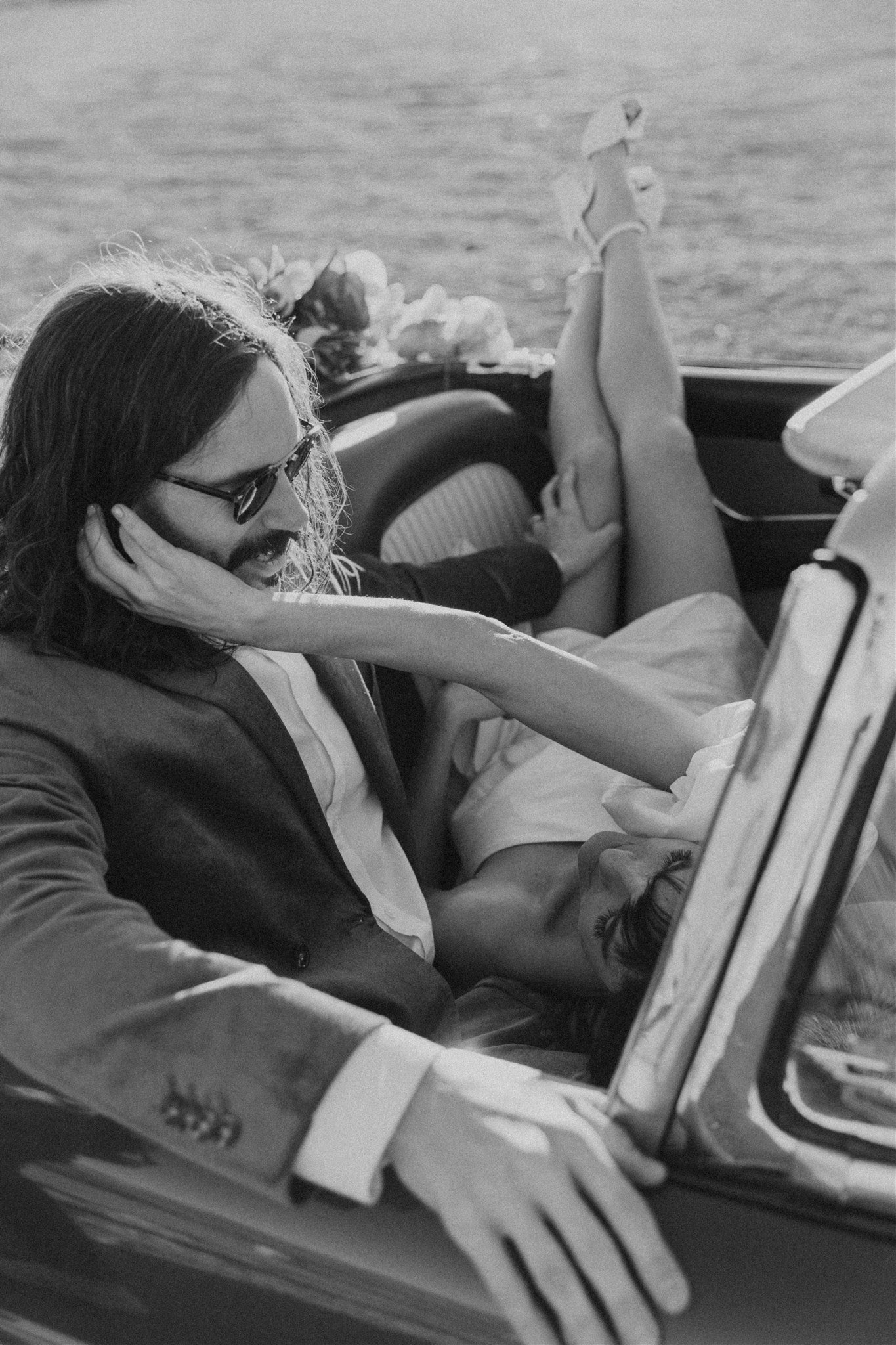black and white styled photograph with relaxed couple posing in a vintage vehicle alongside ocean front road