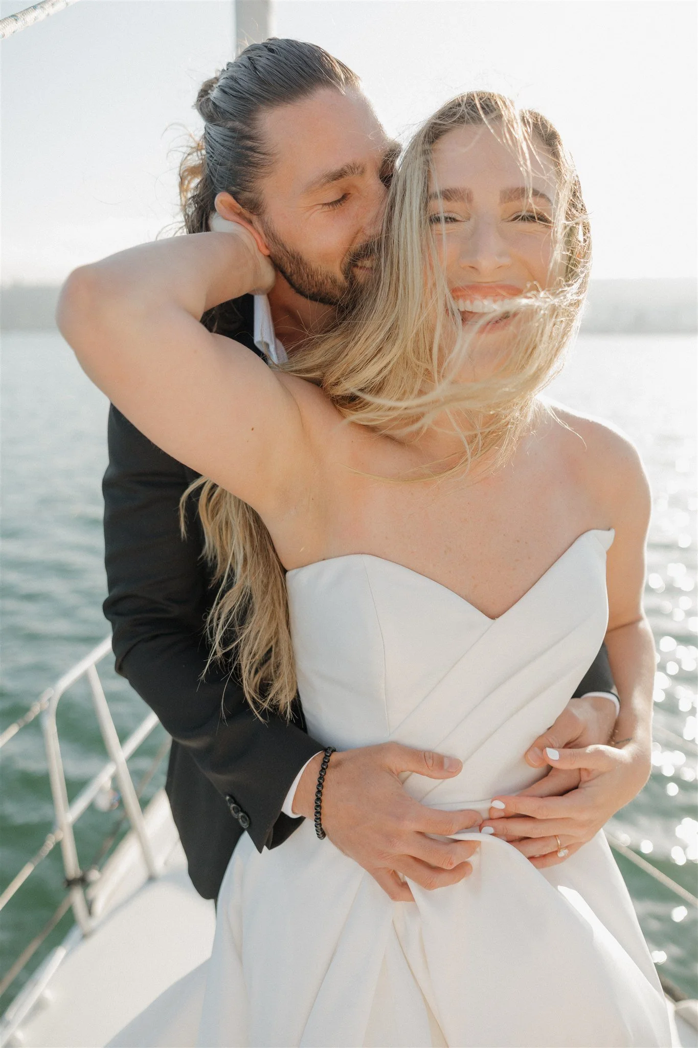 Couple wearing wedding attire, suit and wedding dress,  on a sail boat in the ocean.
