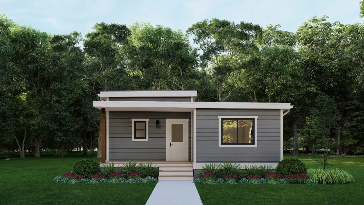 Small modern house with gray siding, white trim, and large windows, surrounded by a green lawn and garden in a wooded area.