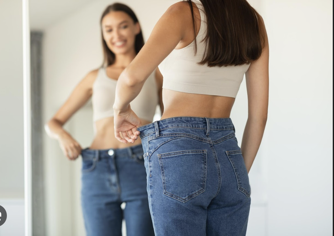 woman looking in the mirror with jeans that are now too big
